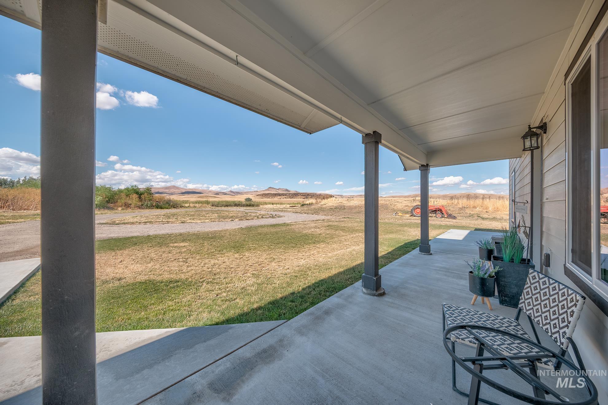 Covered concrete porch extending the length of the home, featuring multiple support columns, a ceiling fan, and exterior wall lanterns