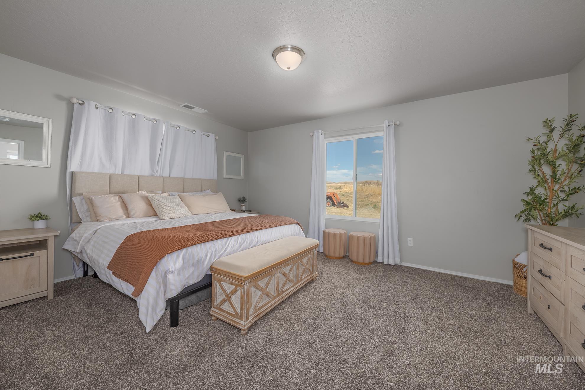 Spacious bedroom featuring light gray wall paint and a large window with white curtain panels