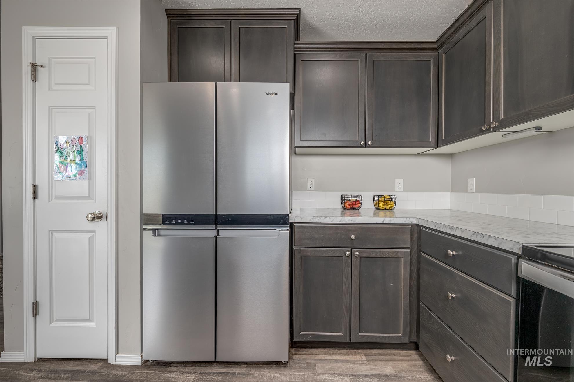 Kitchen featuring dark wood-finish cabinetry, stainless steel appliances, light-toned countertops, and a white subway tile backsplash