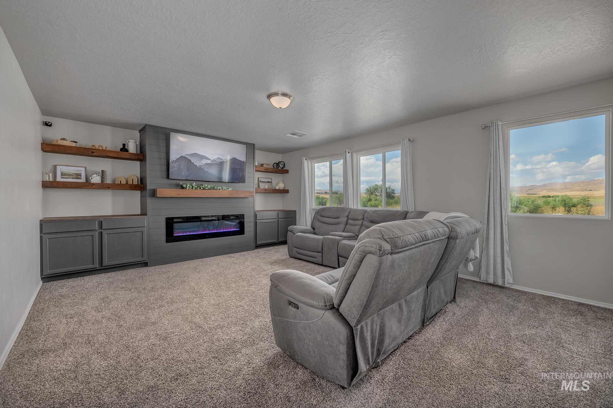 Living area featuring a textured gray accent wall with an electric fireplace, a wood-finish mantel, and built-in cabinetry with open shelving