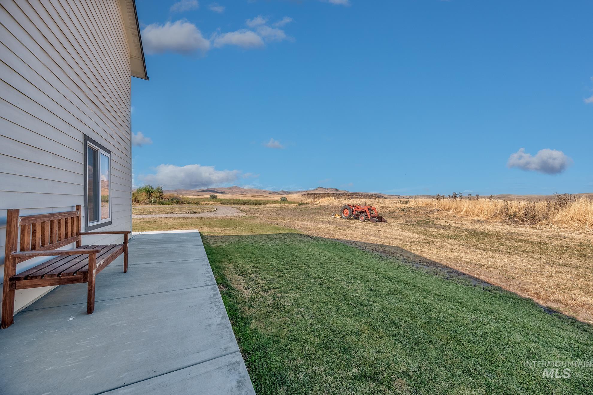 Expansive side yard featuring a concrete patio, manicured lawn, and distant open fields with rolling hills