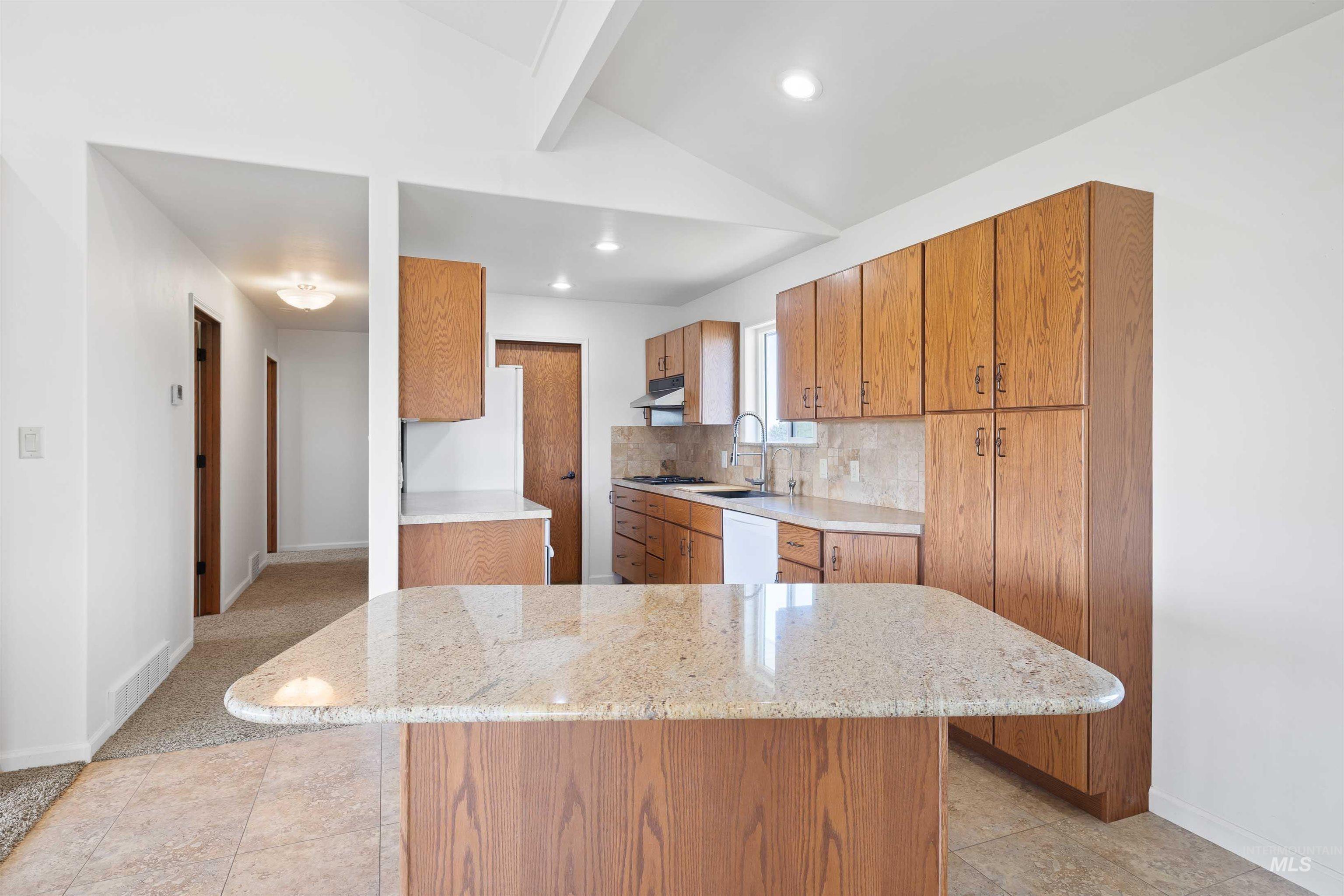 Kitchen featuring brown cabinetry, backsplash, light stone counters, fridge, and recessed lighting