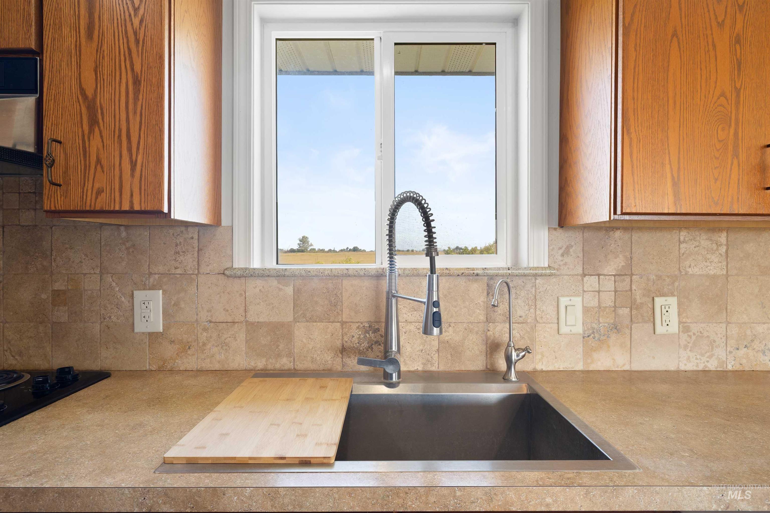 Kitchen with decorative backsplash, brown cabinetry, and ventilation hood