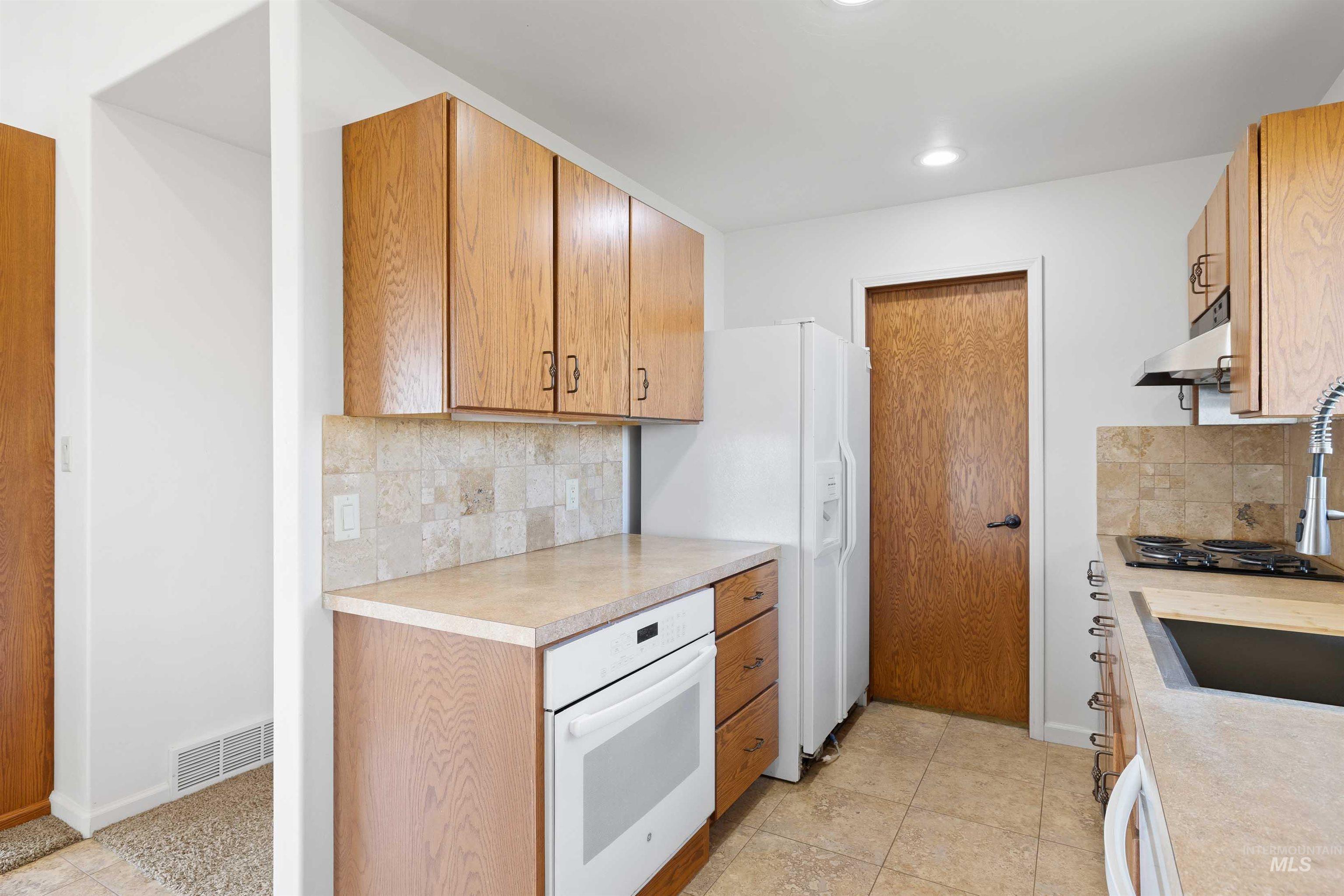 Kitchen with white appliances, light countertops, decorative backsplash, recessed lighting, and under cabinet range hood