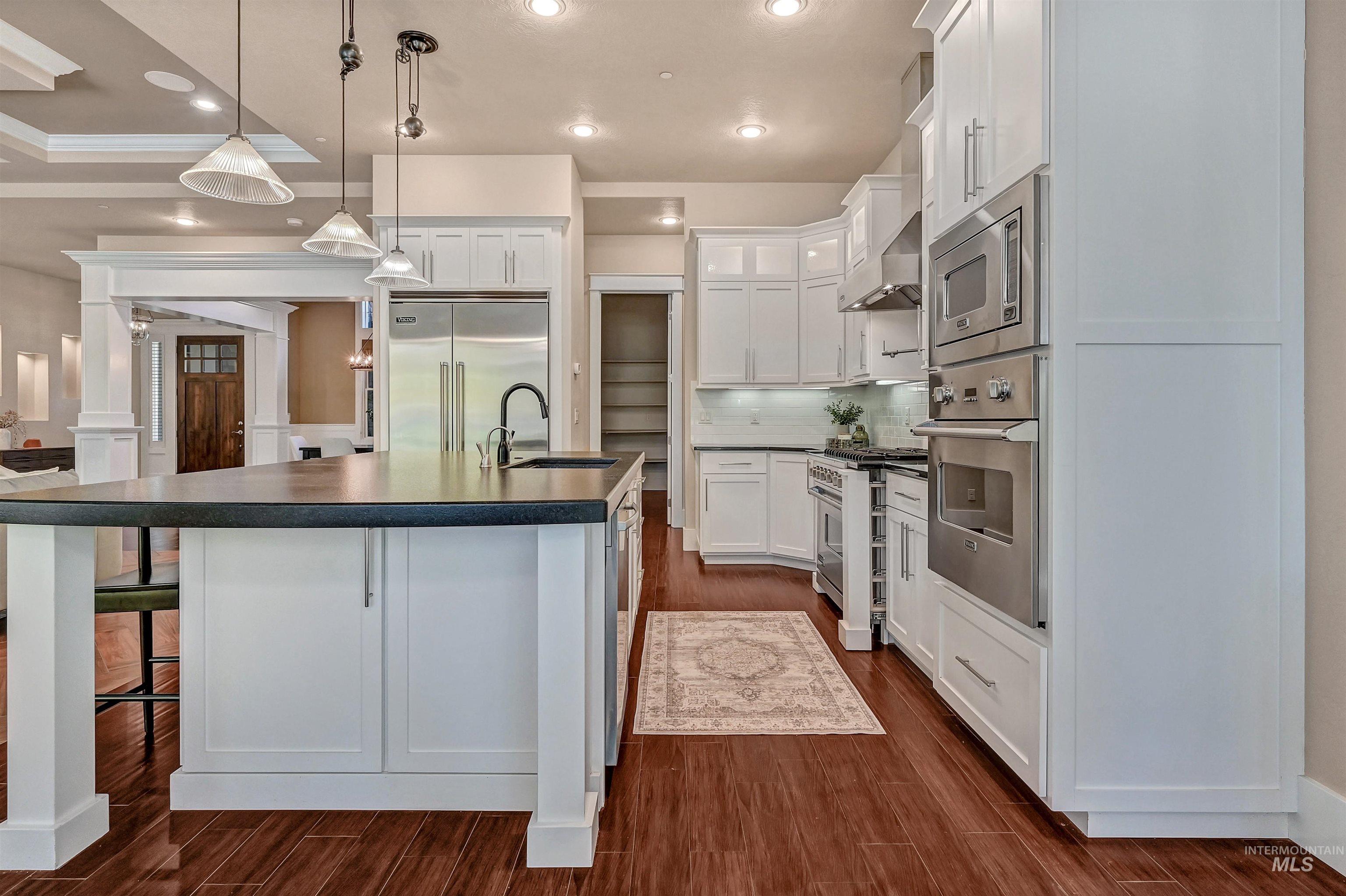 Kitchen featuring dark countertops, hanging light fixtures, built in appliances, a breakfast bar area, and white cabinets