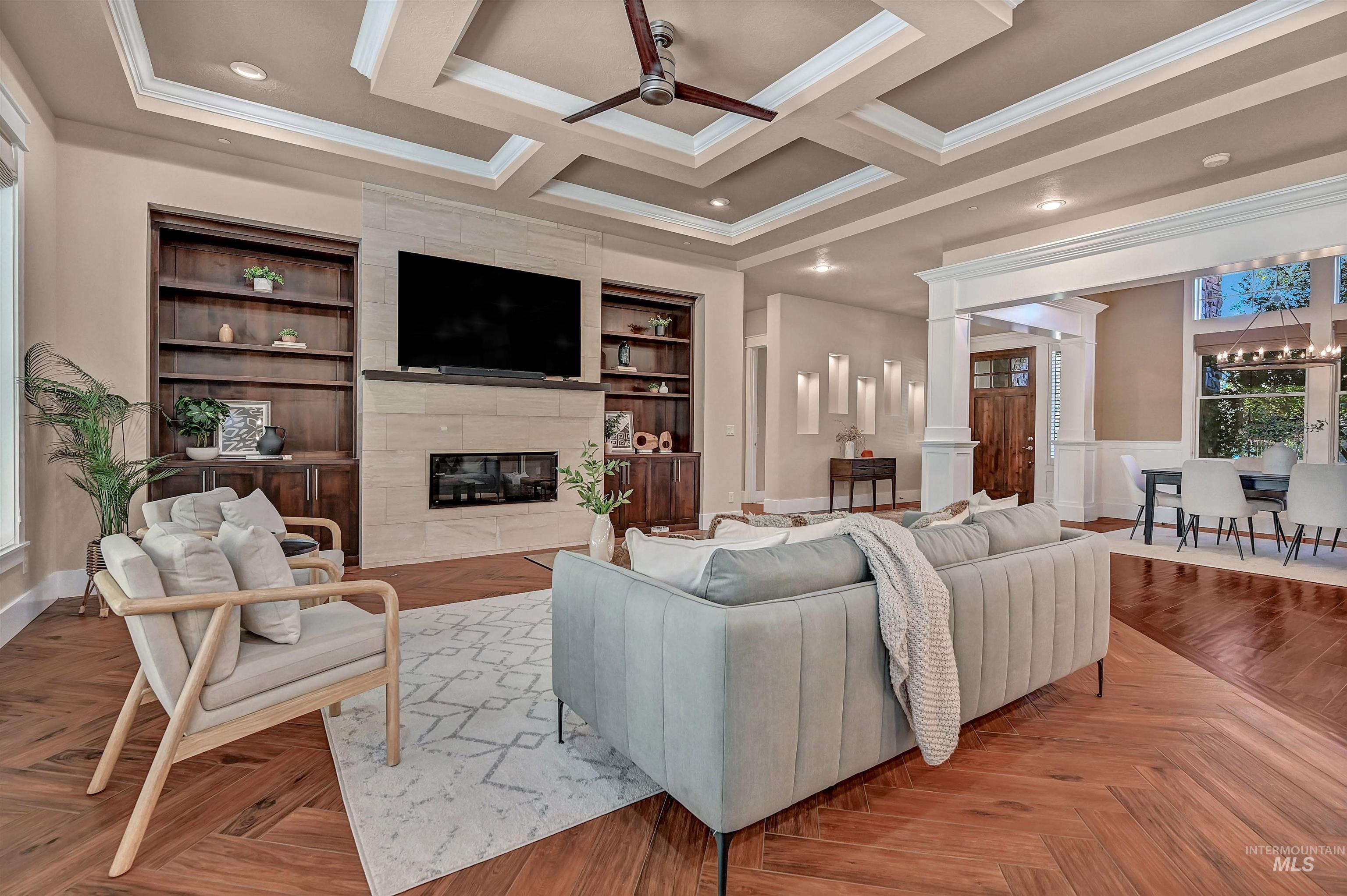 Living area with a tile fireplace, a ceiling fan, decorative columns, crown molding, and coffered ceiling