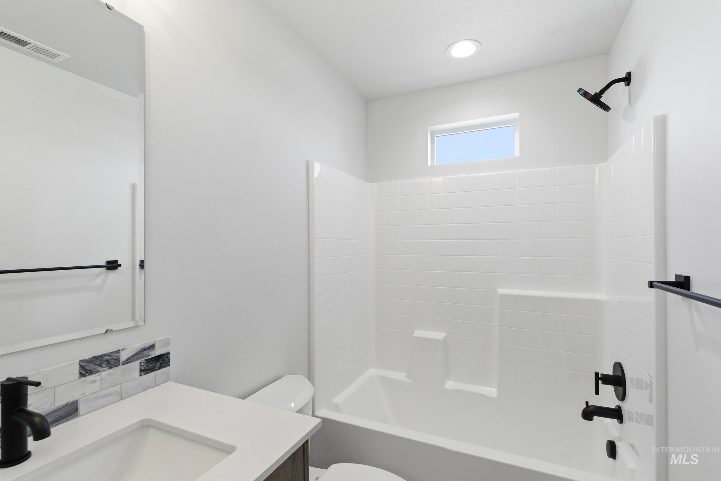 Bathroom featuring a white subway tile-patterned shower surround, a compact window, black fixtures, and a vanity with a rectangular sink and a patterned backsplash