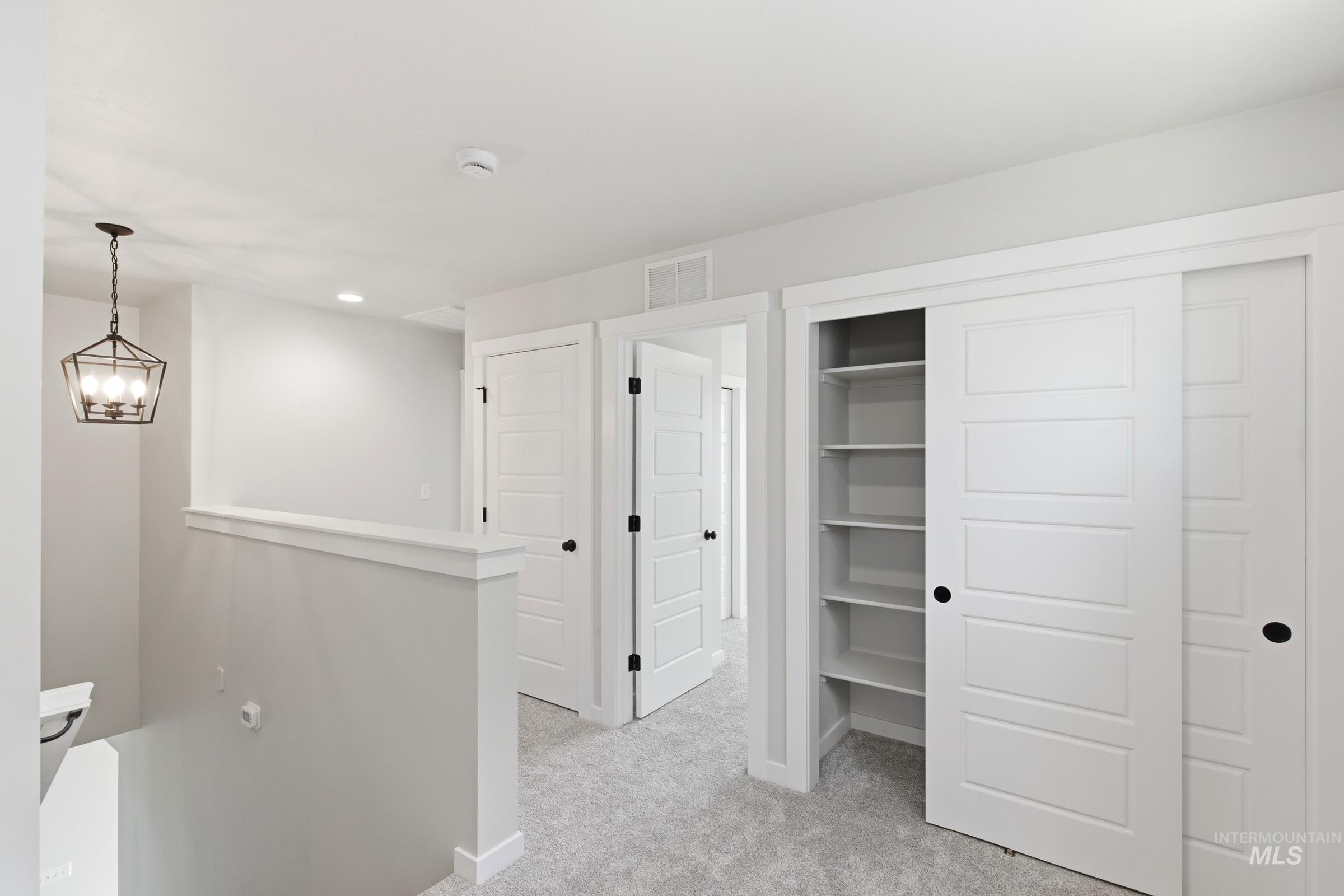 Upper-level hallway featuring light gray walls, plush gray carpeting, and a modern geometric pendant light fixture
