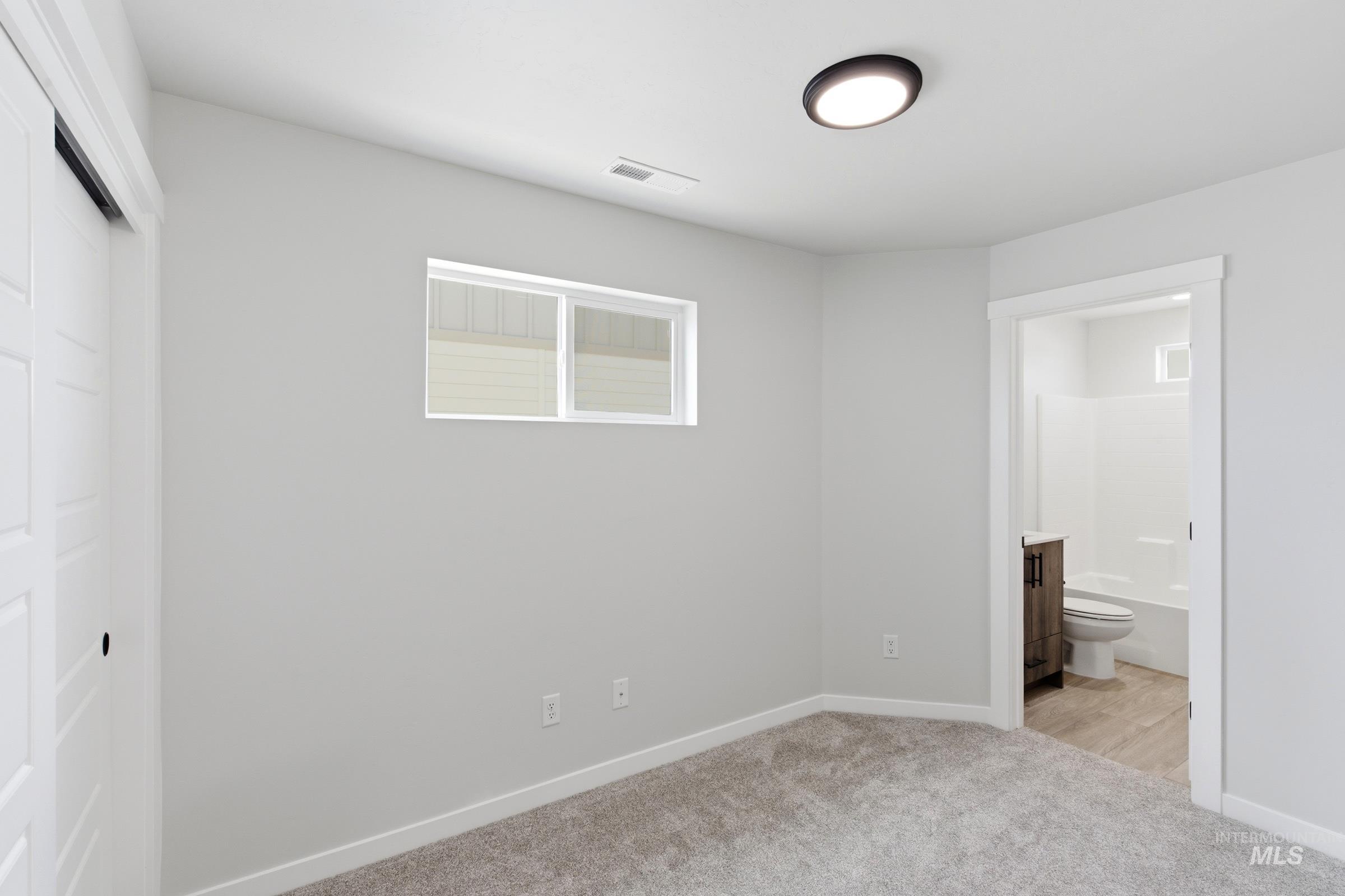 Neutral wall tones complement plush carpeting, a white trim window, and a modern ceiling light fixture