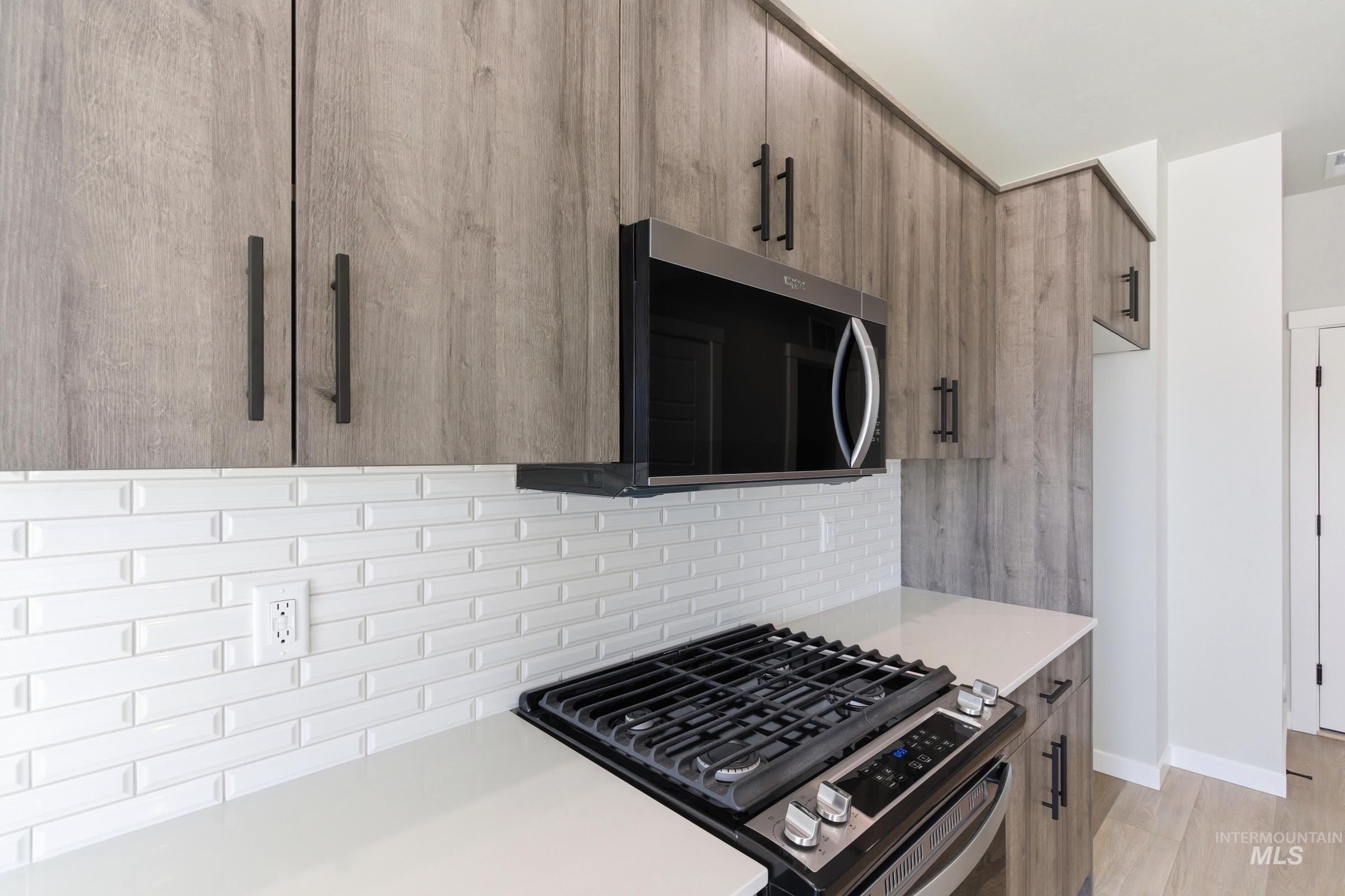 Kitchen featuring a gas range, over-the-range microwave, light wood-finish cabinetry with matte black pulls, white subway tile backsplash, and light countertops