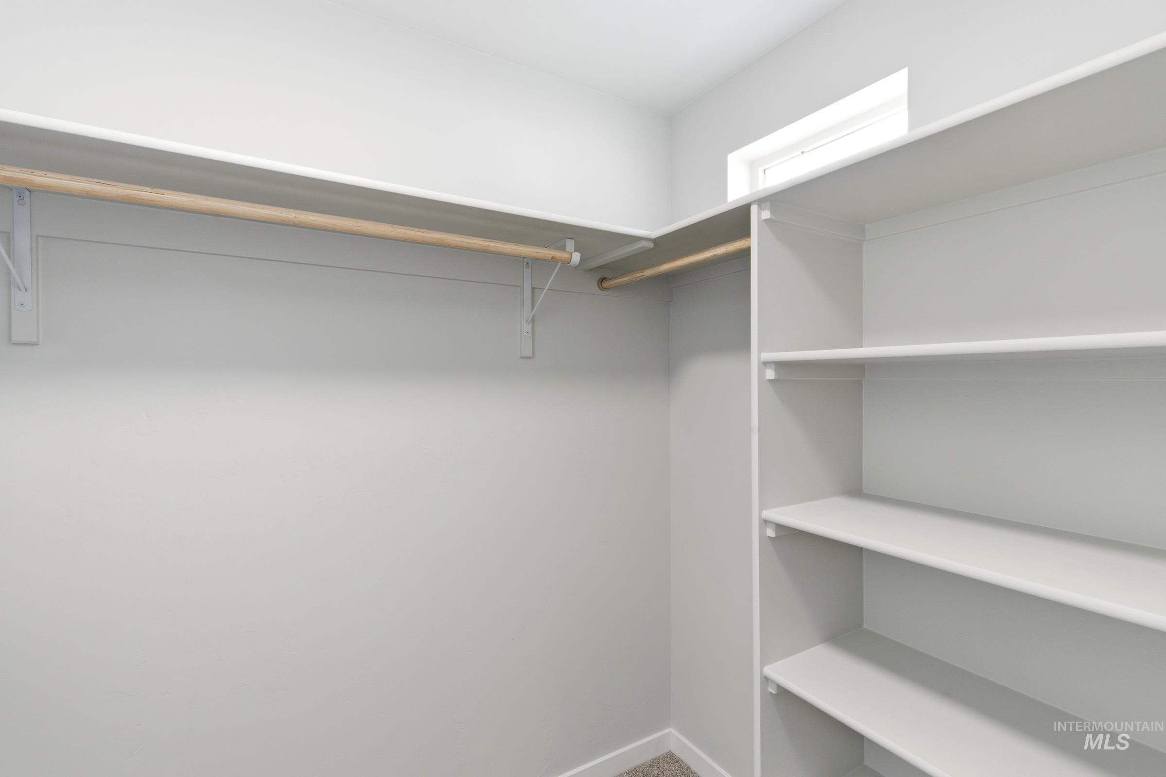 Walk-in closet featuring built-in shelving, two hanging rods, and a window for natural light