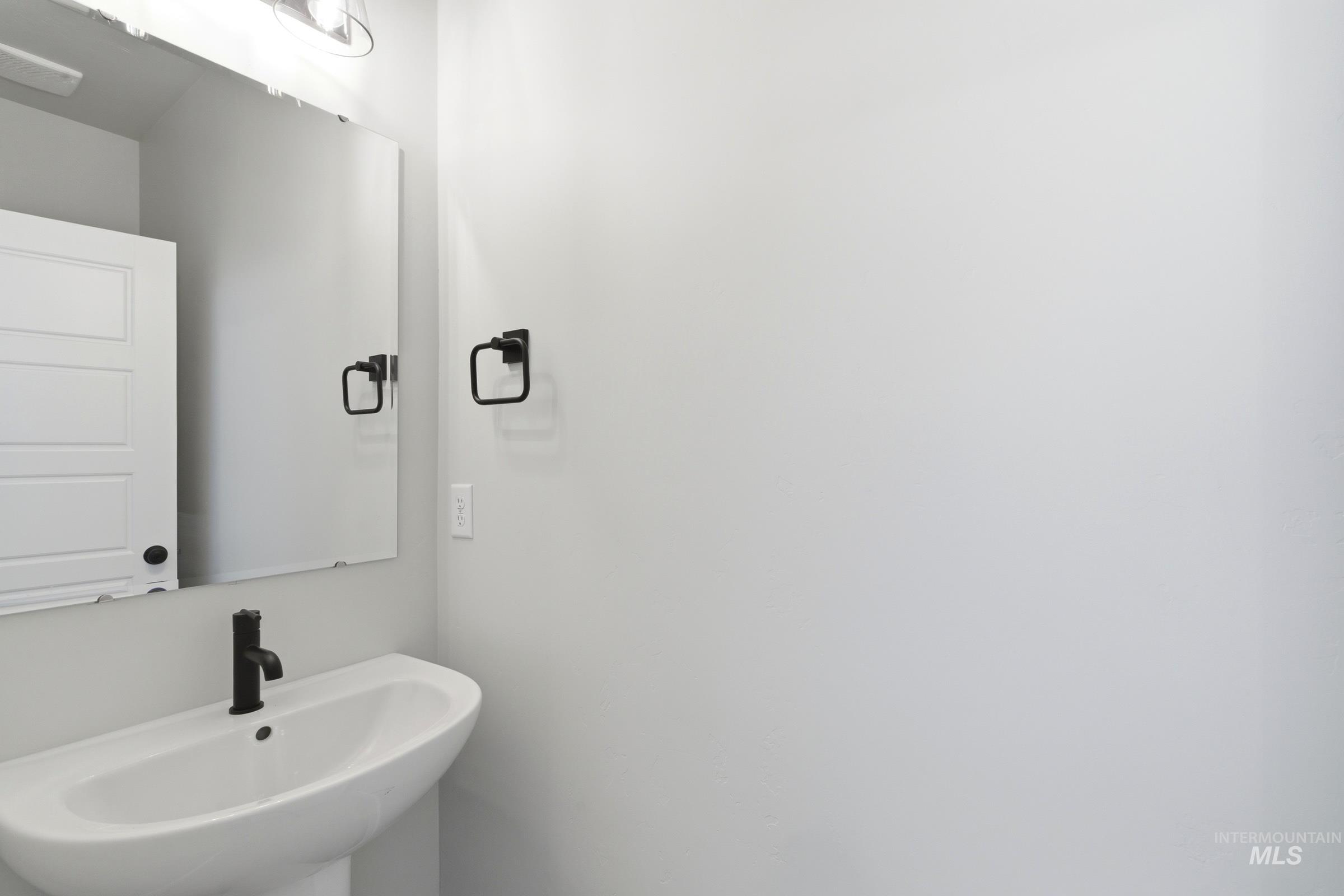 Pedestal sink with matte black faucet, wall-mounted mirror, and integrated lighting fixture