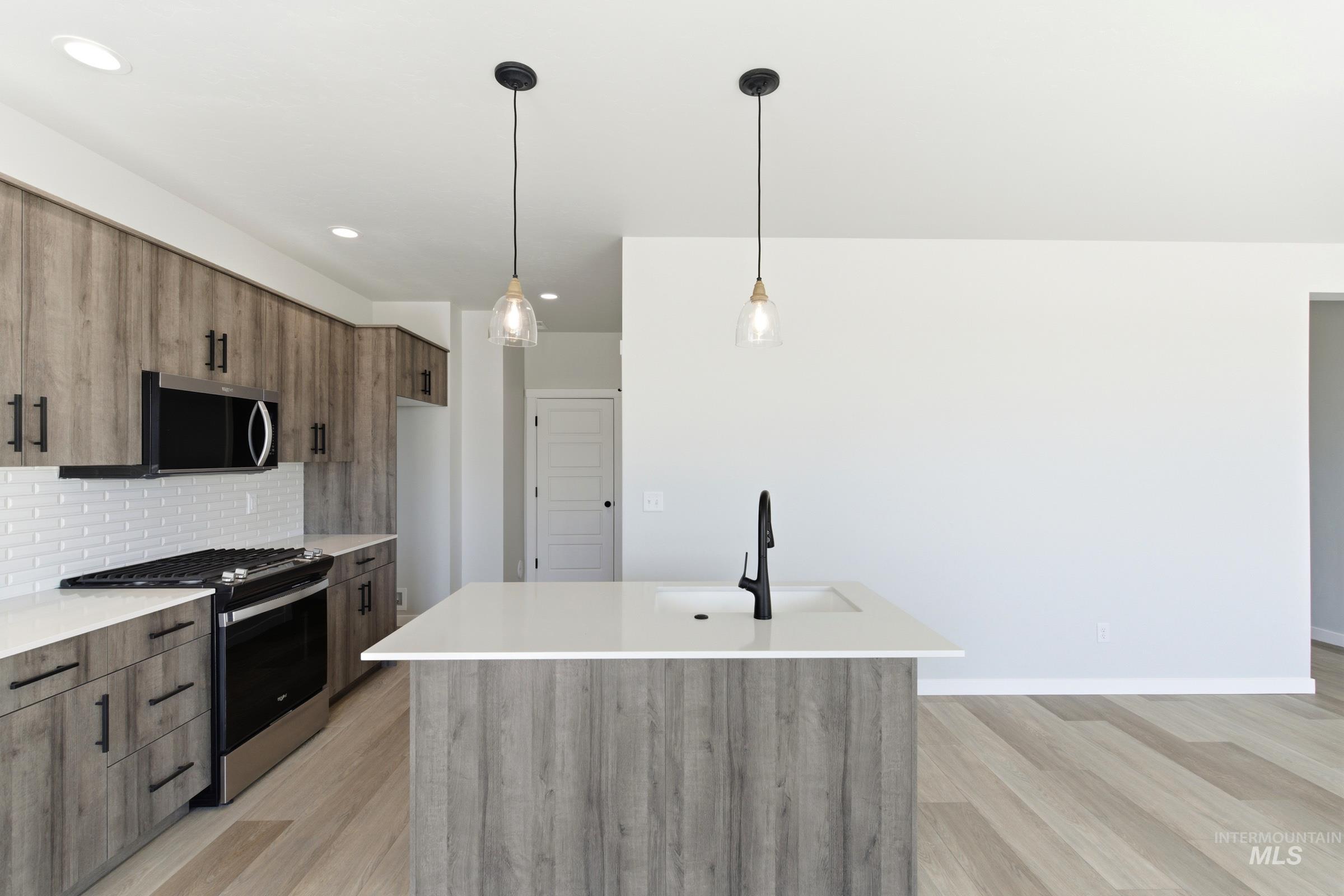 Contemporary kitchen featuring a substantial island with a basin sink and matte black faucet, wood-finish flooring, and pendant lighting