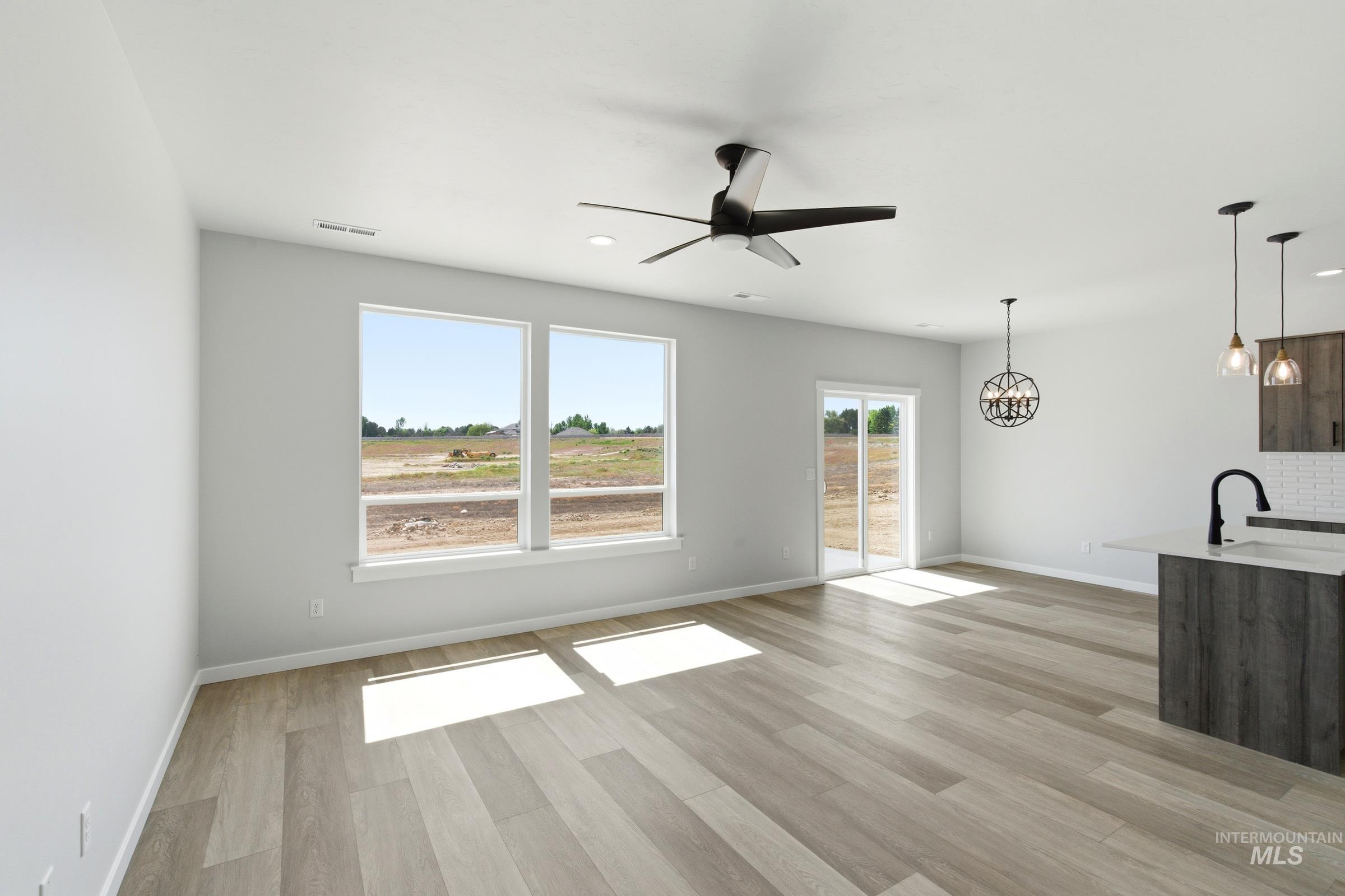 Spacious room featuring light wood-finish flooring, multiple large windows, a sliding glass door, and a modern ceiling fan
