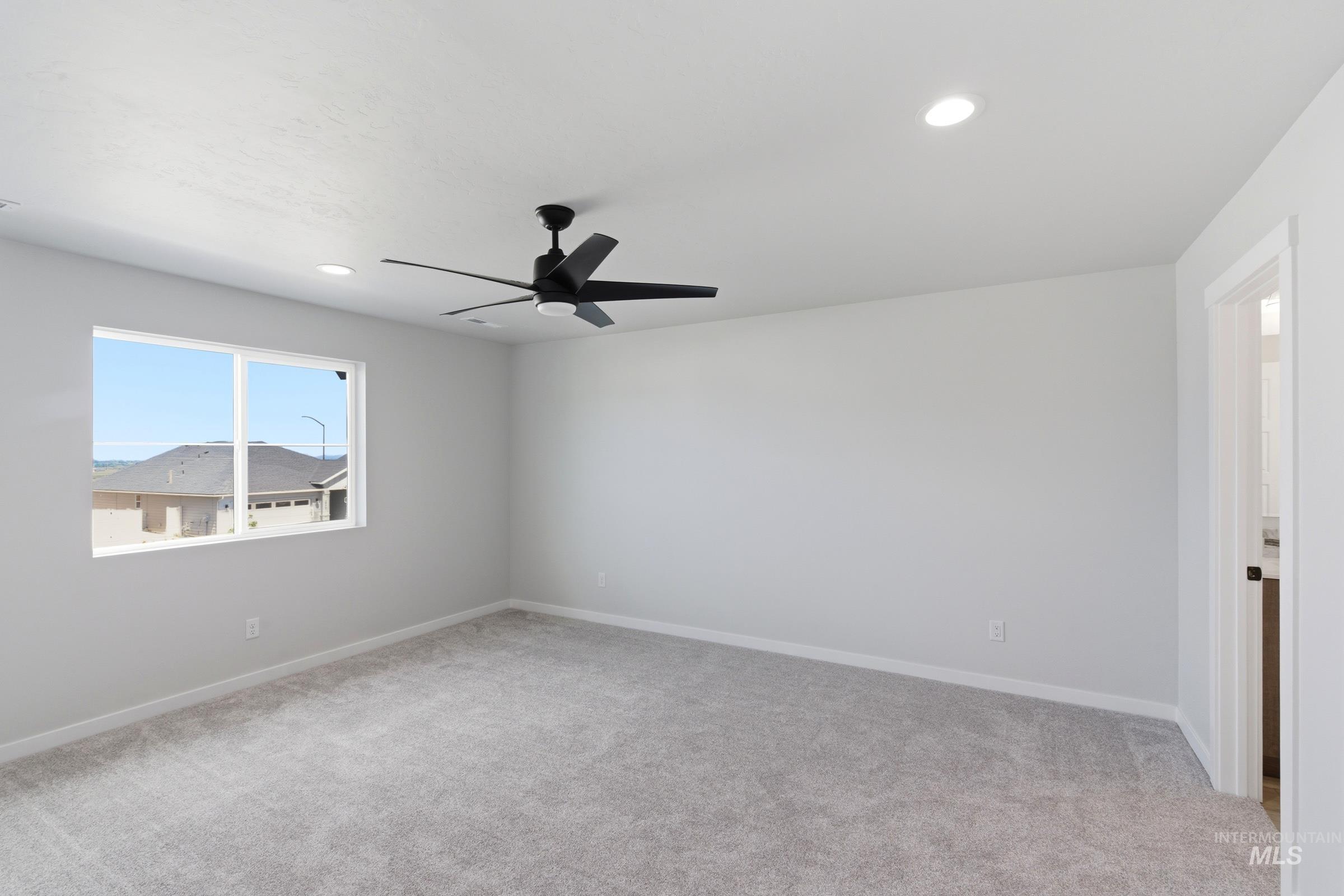 Spacious room featuring light gray carpeting, recessed lighting, a modern black ceiling fan, and large windows providing natural illumination