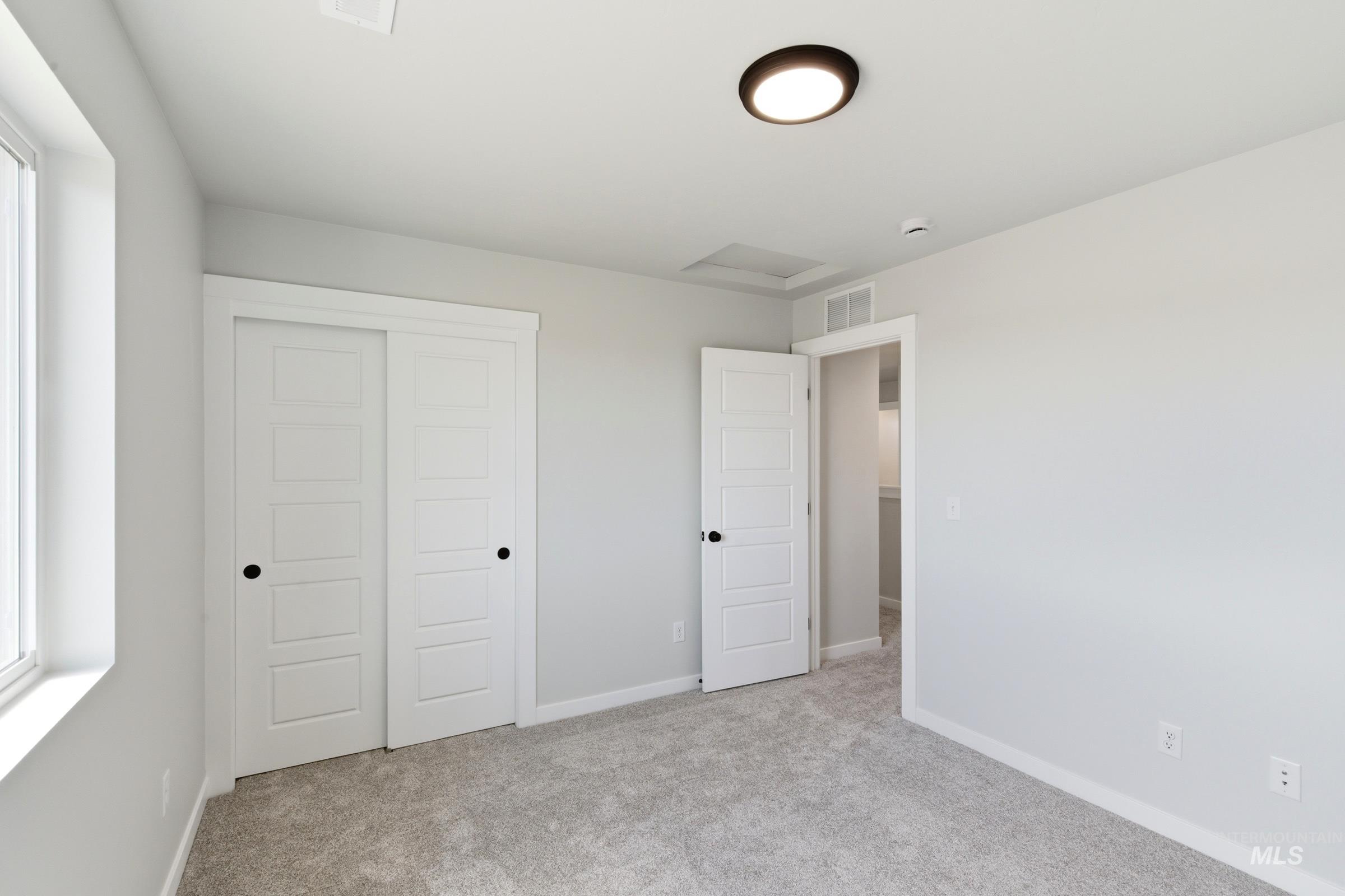 Room featuring light gray wall paint, gray carpeting, a window with white trim, white paneled doors with black hardware, and a flush-mount ceiling light fixture