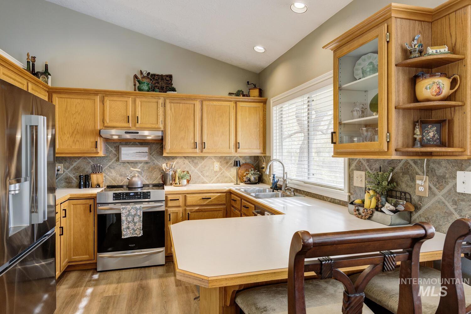 Kitchen featuring light countertops, appliances with stainless steel finishes, open shelves, vaulted ceiling, and light wood finished floors