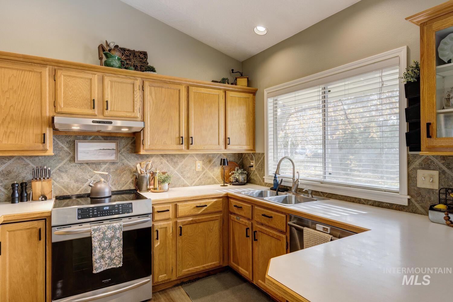 Kitchen featuring light countertops, stainless steel appliances, decorative backsplash, under cabinet range hood, and vaulted ceiling