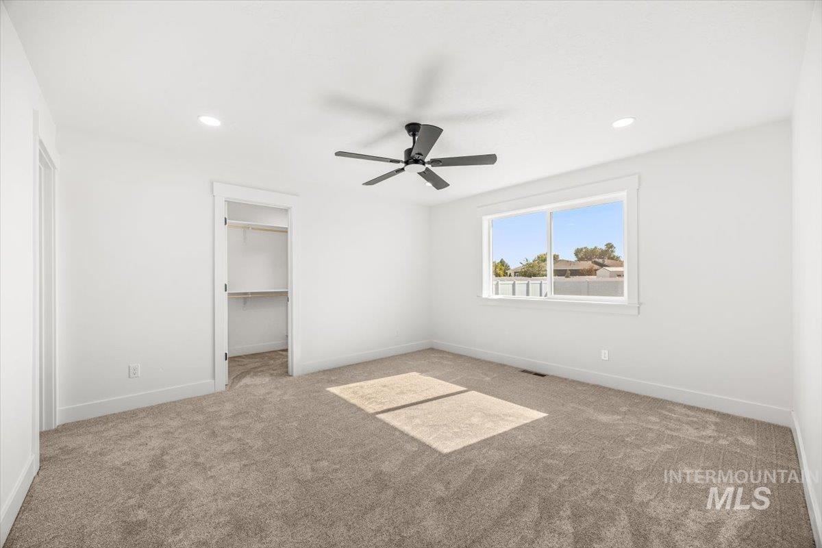 Unfurnished bedroom with light carpet, a spacious closet, ceiling fan, and recessed lighting