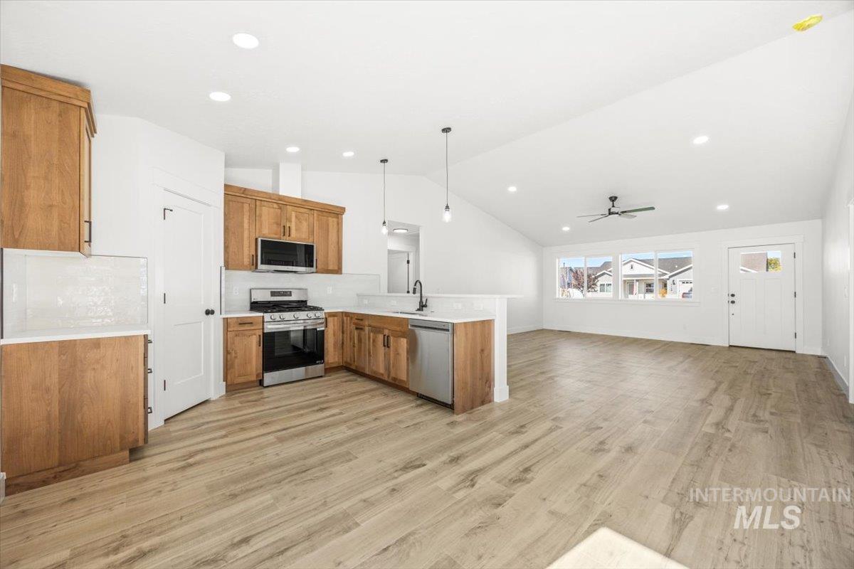 Kitchen with pendant lighting, backsplash, appliances with stainless steel finishes, open floor plan, and a peninsula