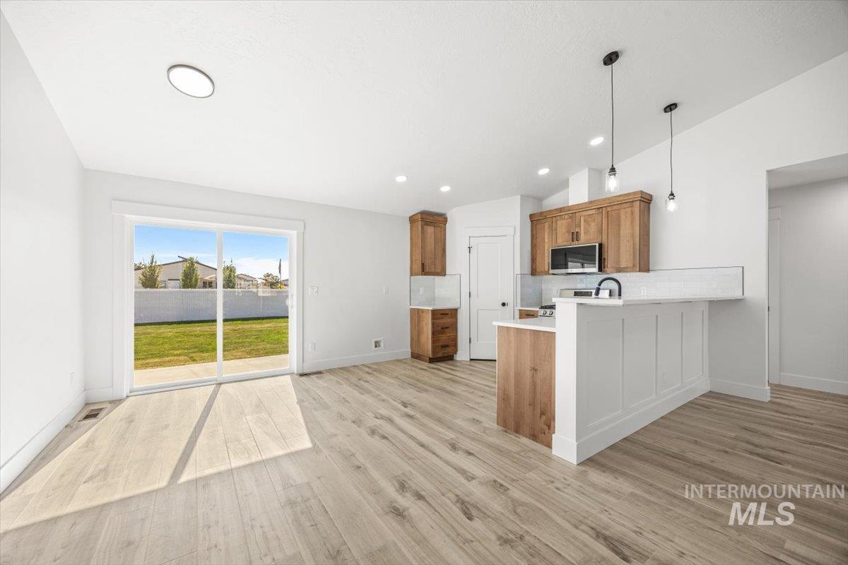 Kitchen with brown cabinetry, backsplash, pendant lighting, a peninsula, and light countertops
