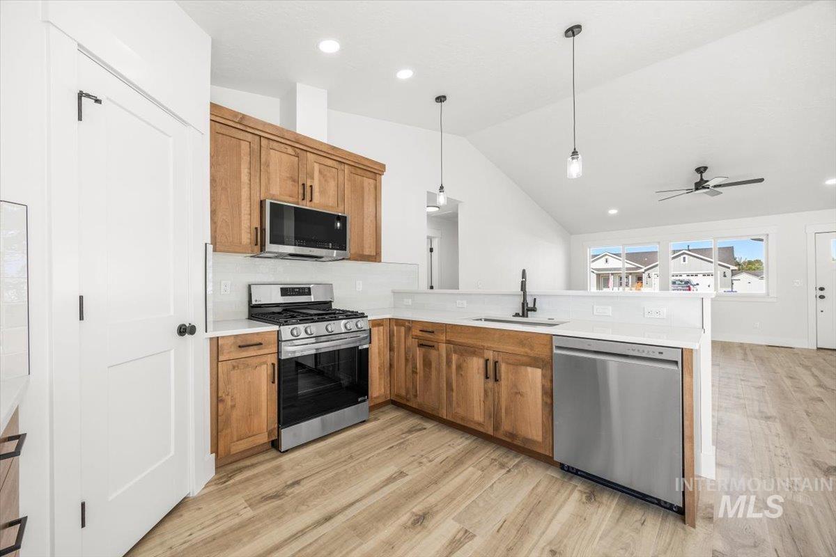 Kitchen with brown cabinets, stainless steel appliances, lofted ceiling, hanging light fixtures, and recessed lighting