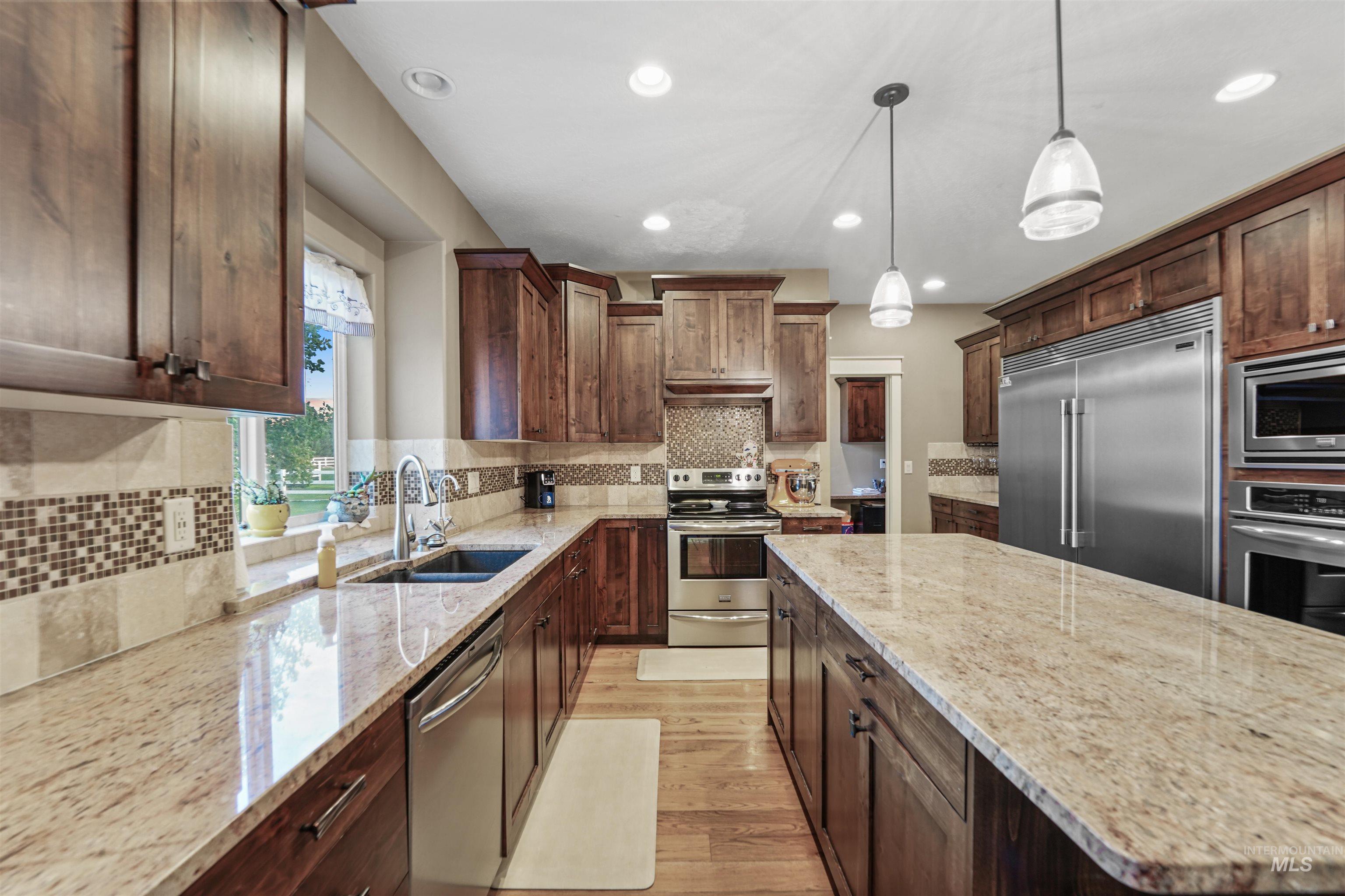 Kitchen with built in appliances, light stone counters, light wood-style flooring, pendant lighting, and tasteful backsplash