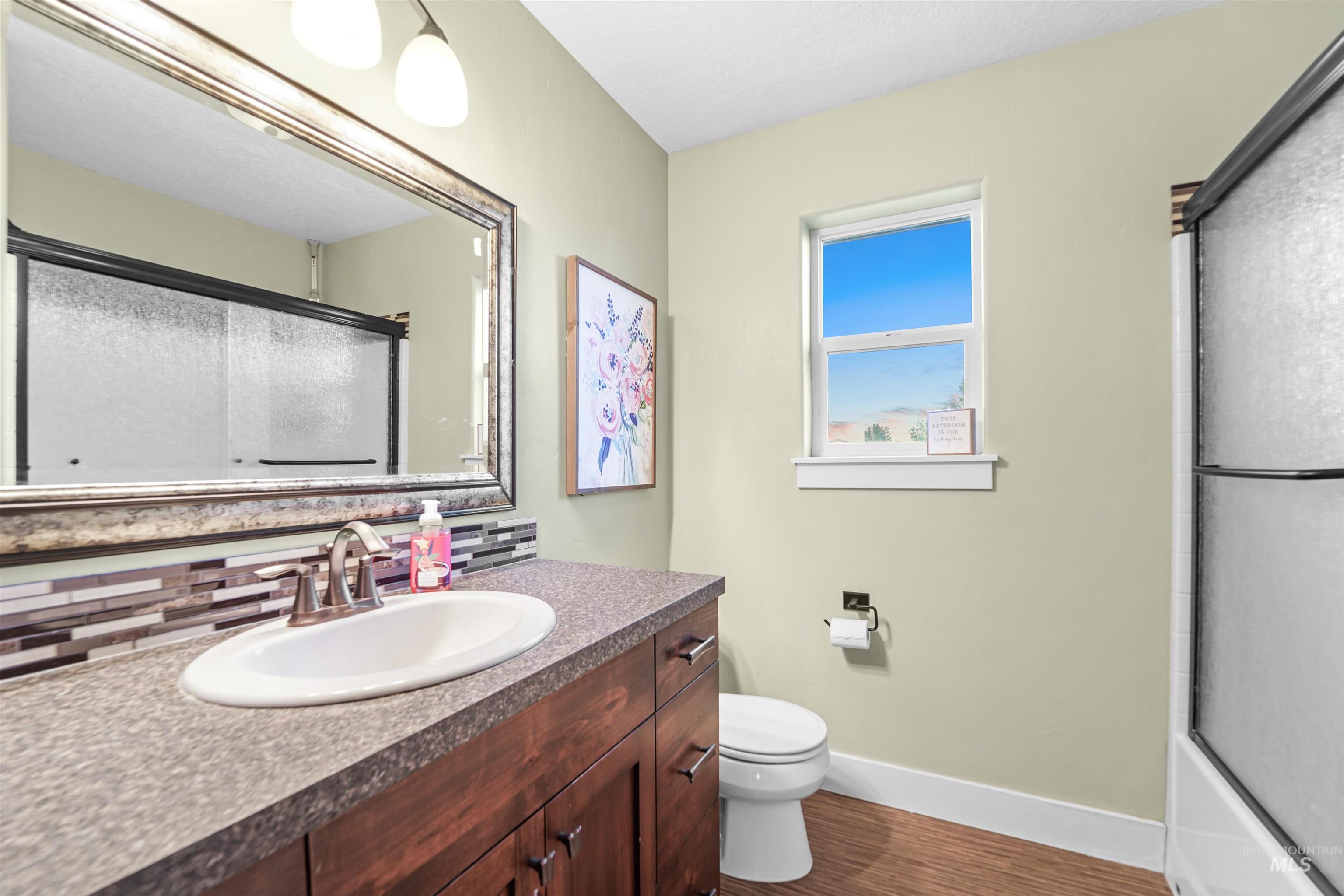 Bathroom featuring vanity, dark wood-style floors, enclosed tub / shower combo, and decorative backsplash