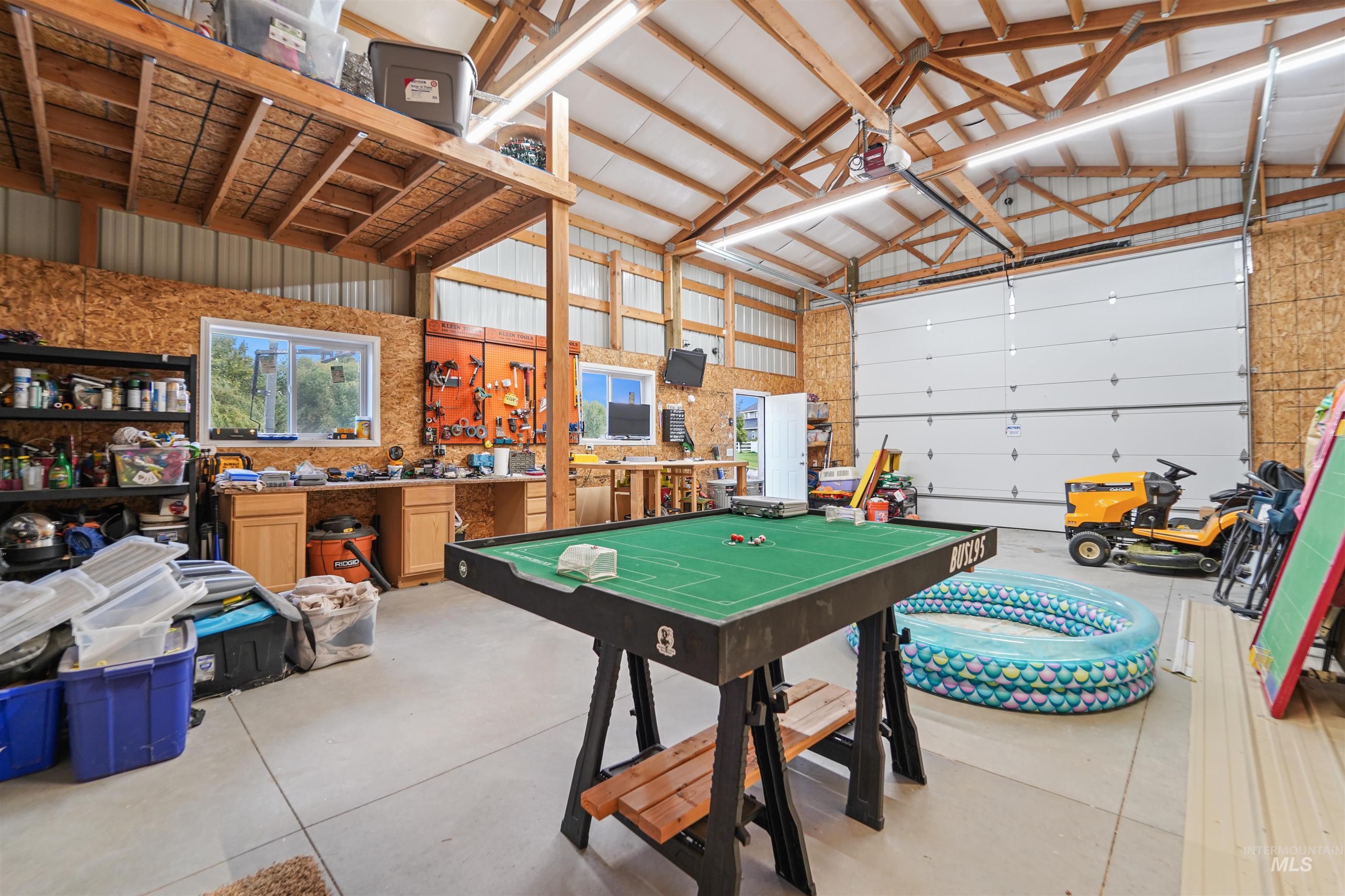Game room with a garage, high vaulted ceiling, metal wall, and a workshop area