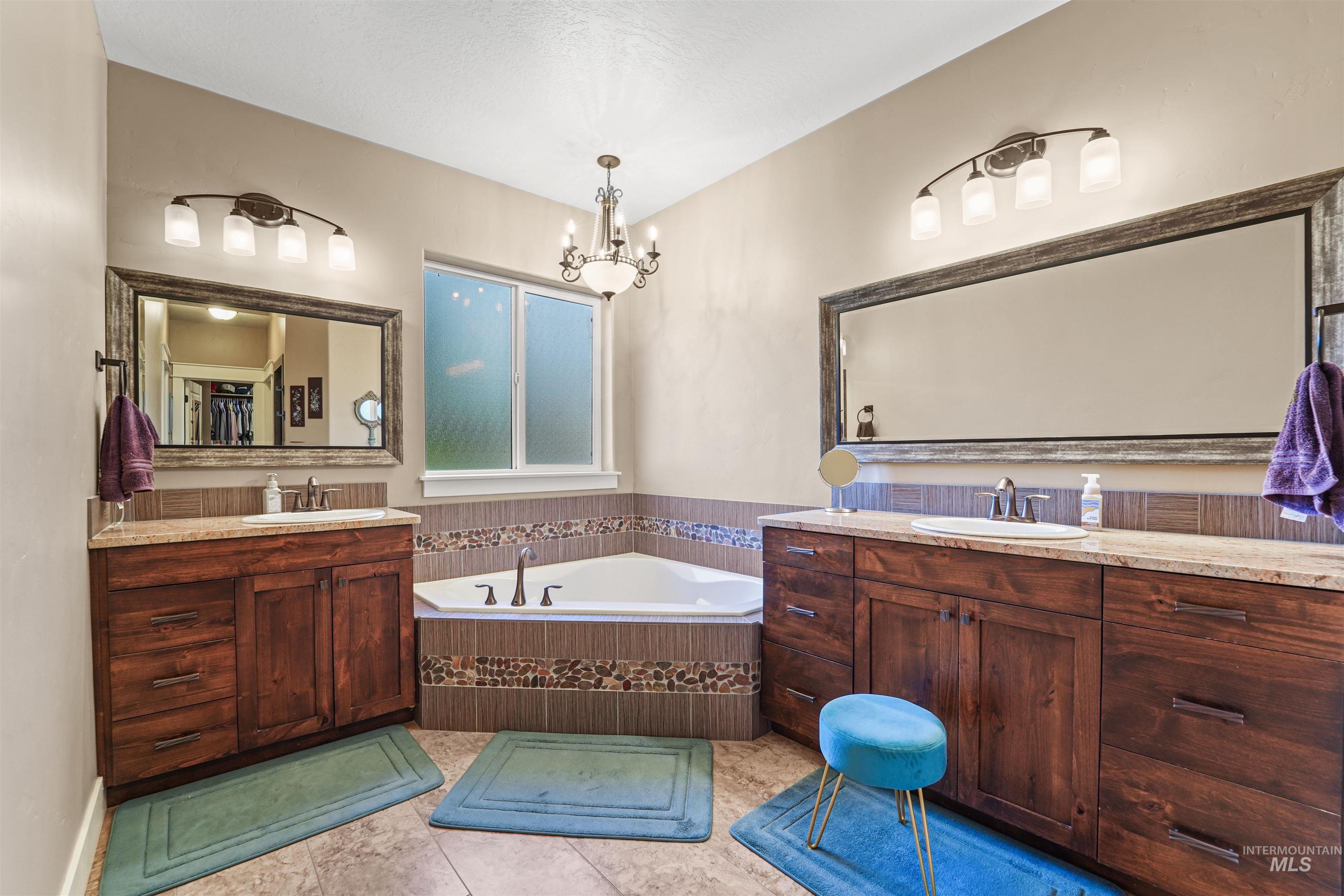 Bathroom with two vanities, a garden tub, light tile patterned floors, and a chandelier