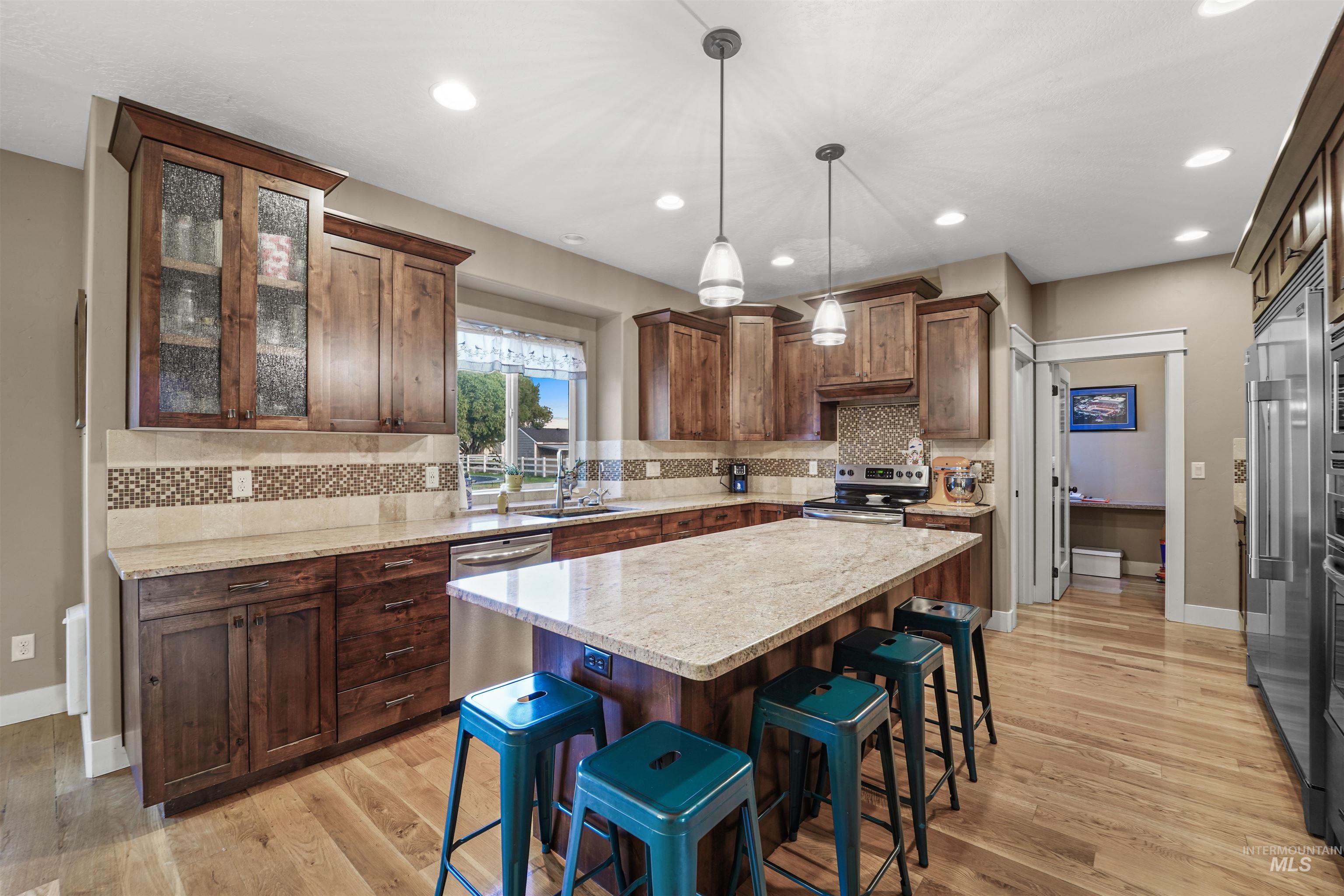 Kitchen with decorative light fixtures, a kitchen breakfast bar, light stone countertops, appliances with stainless steel finishes, and a center island