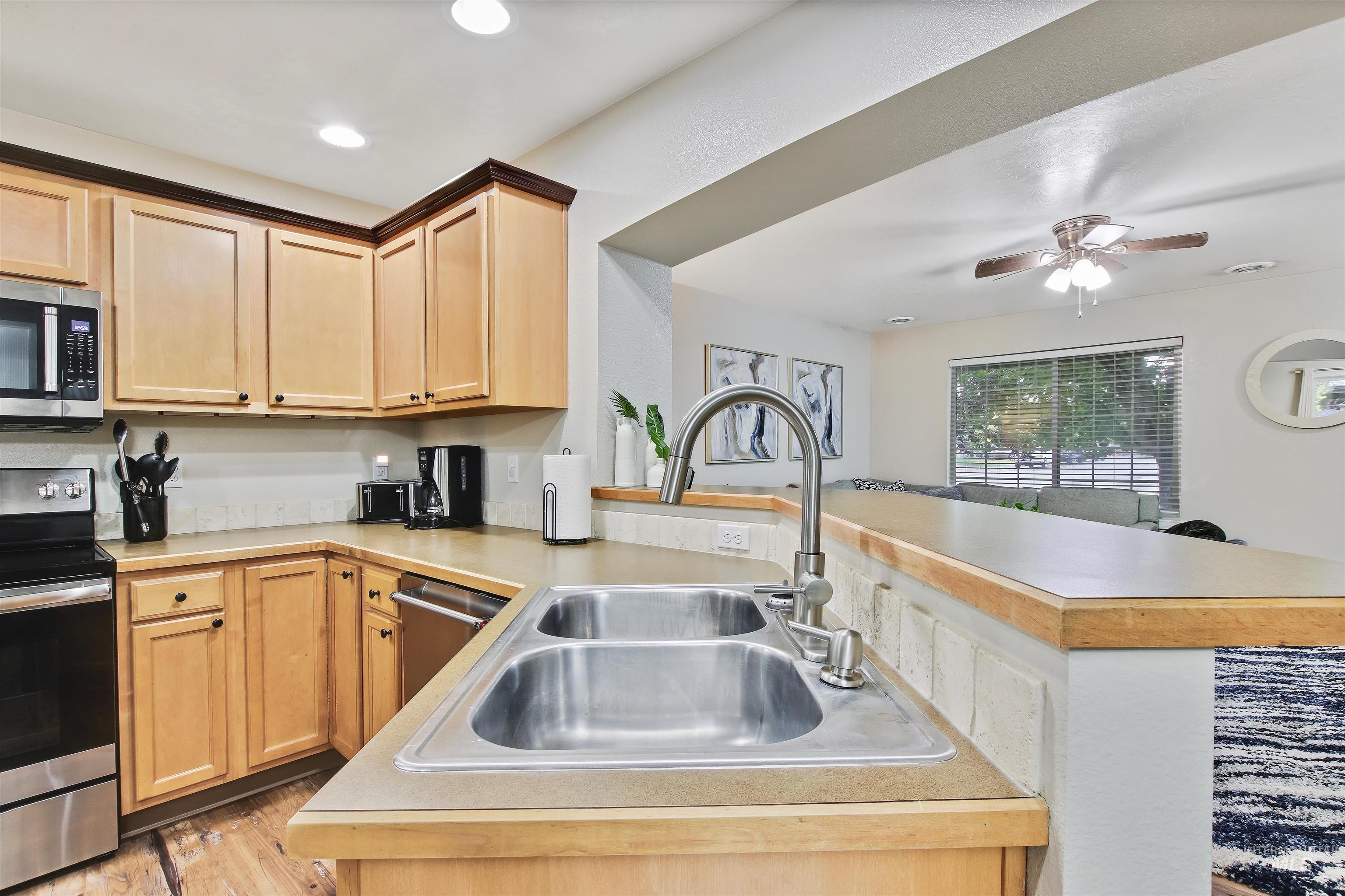 Kitchen featuring appliances with stainless steel finishes, light countertops, light brown cabinets, a ceiling fan, and recessed lighting
