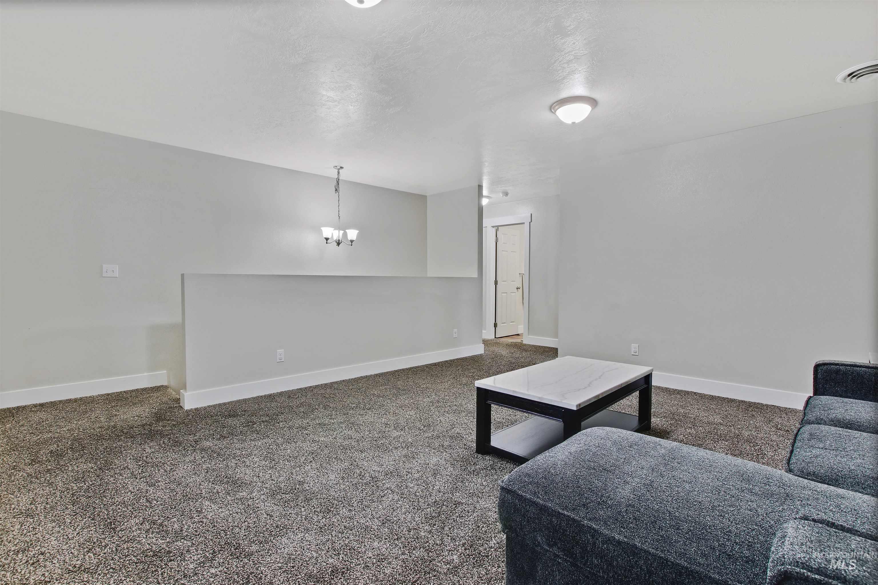 Living room with dark colored carpet, a textured ceiling, and a chandelier