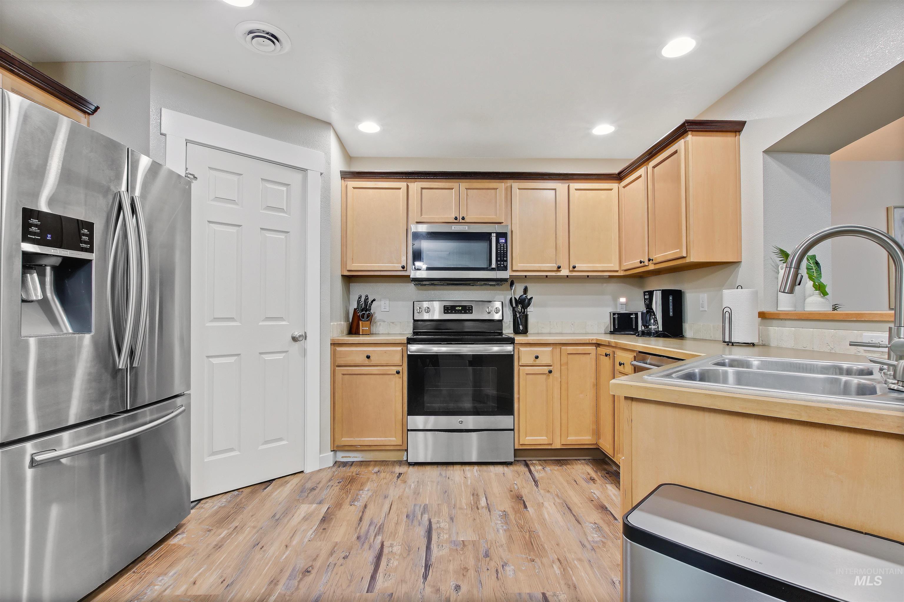 Kitchen with appliances with stainless steel finishes, light brown cabinetry, light wood-style flooring, light countertops, and recessed lighting