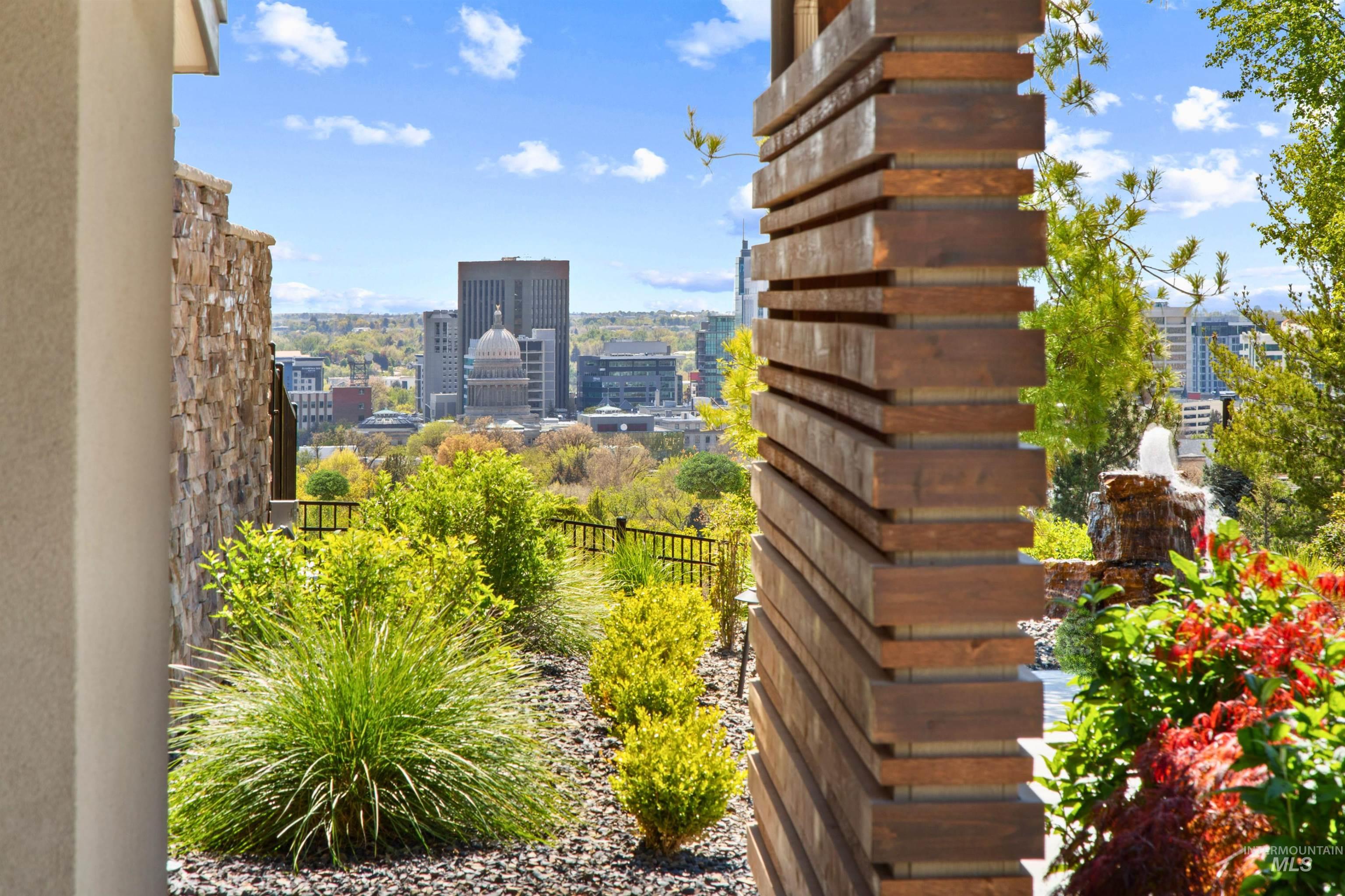 Landscaped outdoor space featuring a stone veneer wall, vertical wood-slat privacy screen, layered plantings, and a multi-tiered fountain