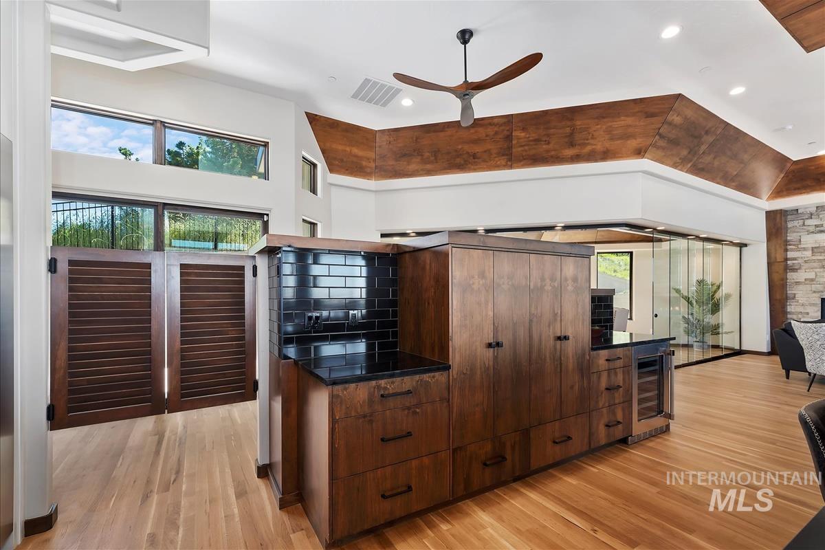 Expansive living area featuring light wood-finish flooring, a built-in wet bar with dark wood cabinetry and black subway tile backsplash, and a contemporary ceiling fan