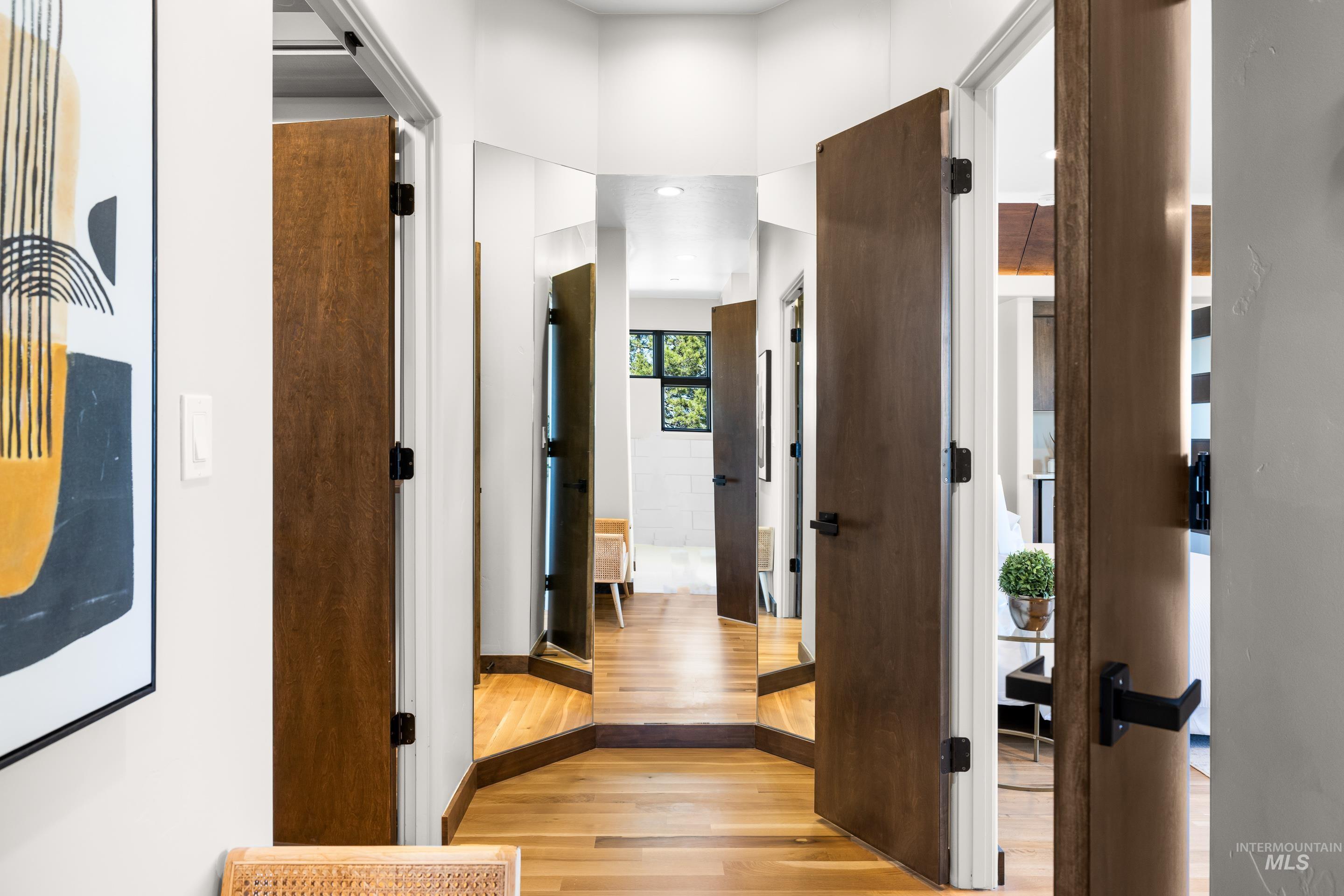Hardwood flooring throughout a hallway featuring solid core doors with matte black hardware