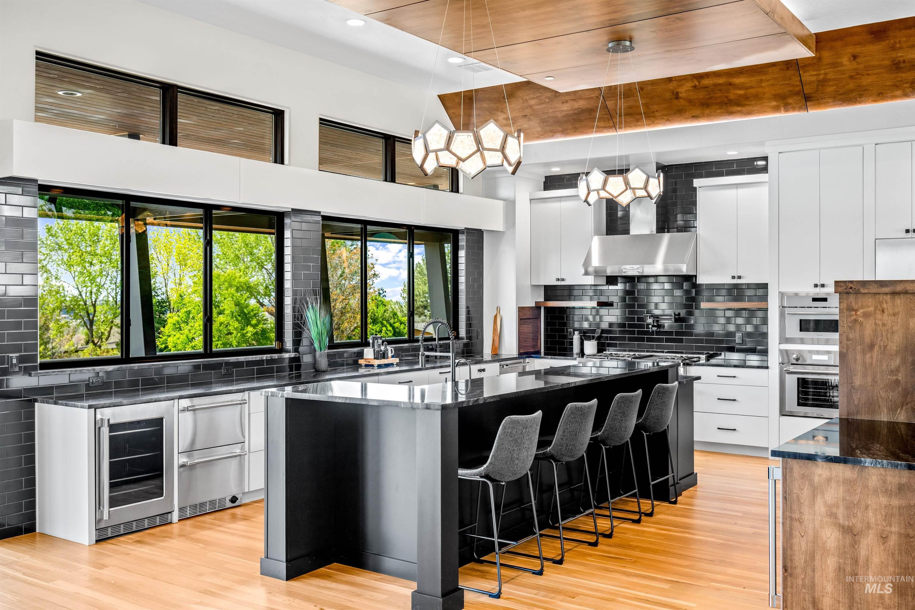 Gourmet kitchen featuring a large central island with seating, integrated stainless steel appliances, dark subway tile backsplash, light wood-finish flooring, and expansive windows