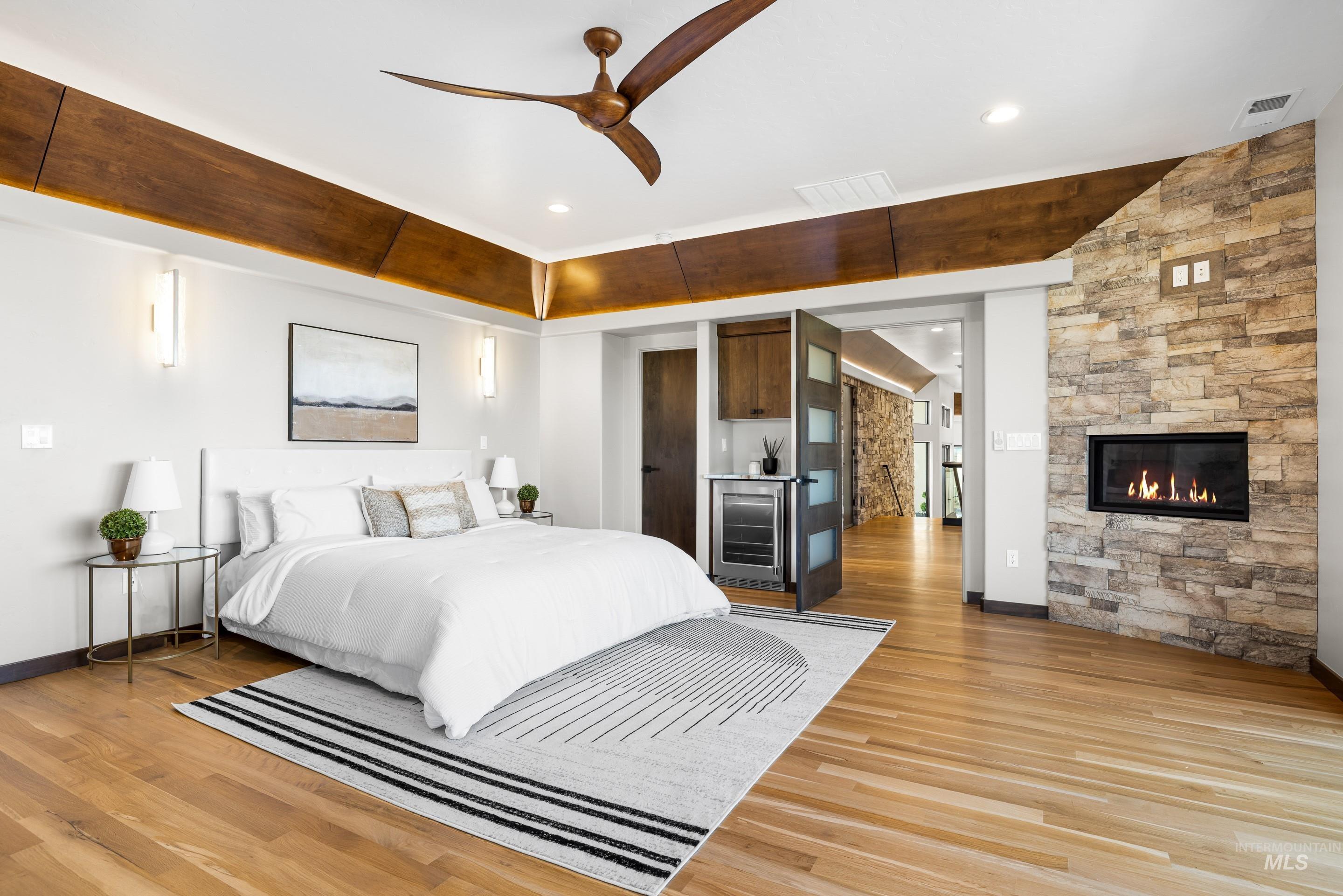 Spacious room featuring wood-finish flooring, a stone-accented wall with an inset fireplace, and a built-in wet bar with a beverage refrigerator