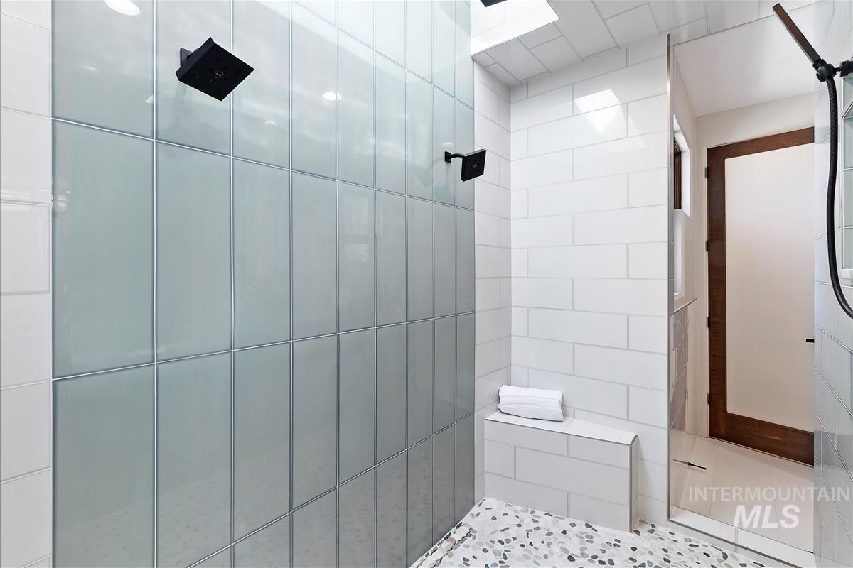 Spacious shower with two matte black rain showerheads, light-colored subway tile walls, and a pebble-finish floor