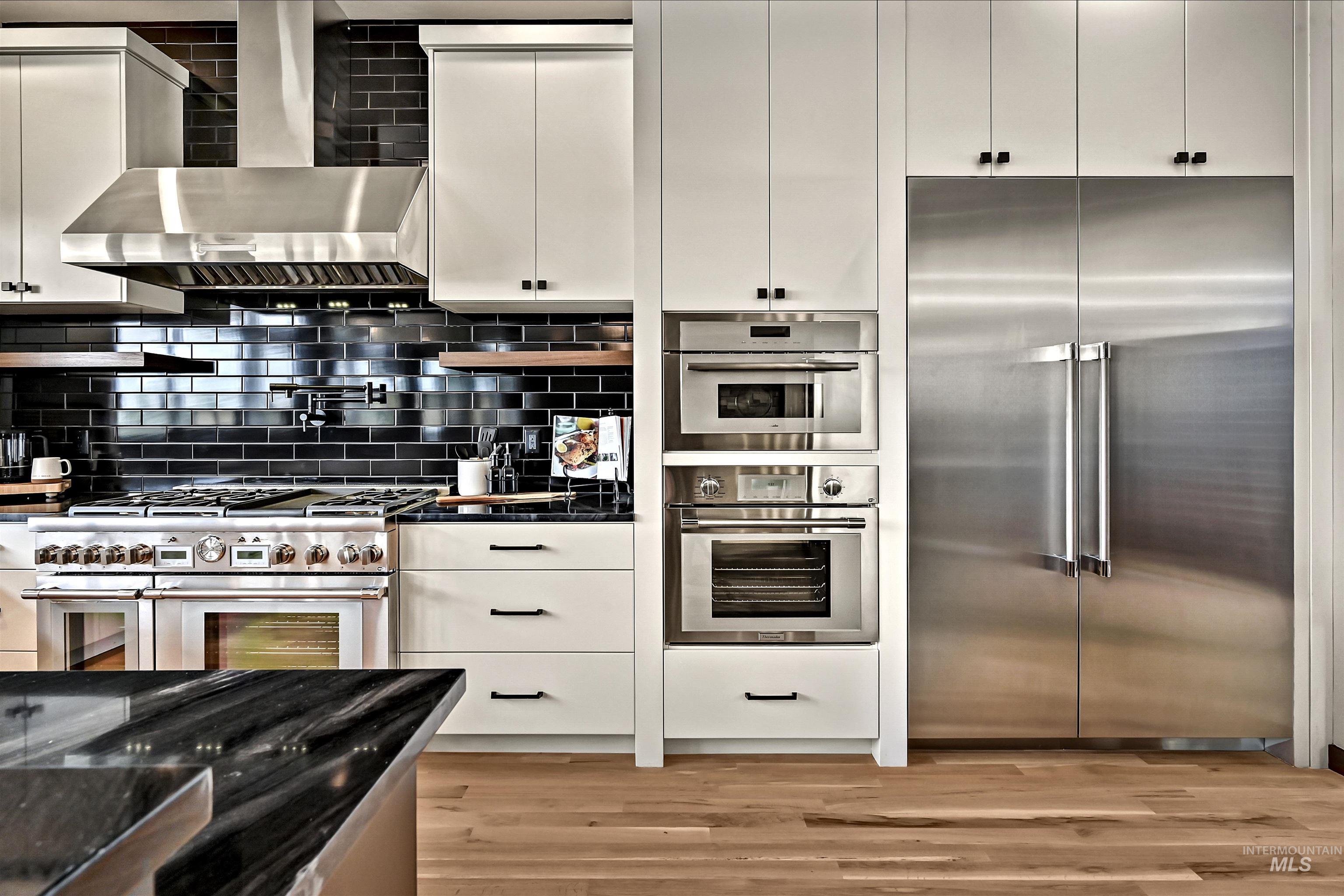 Sleek kitchen featuring a stainless steel range with a matching vent hood, black subway tile backsplash, and light wood-finish flooring