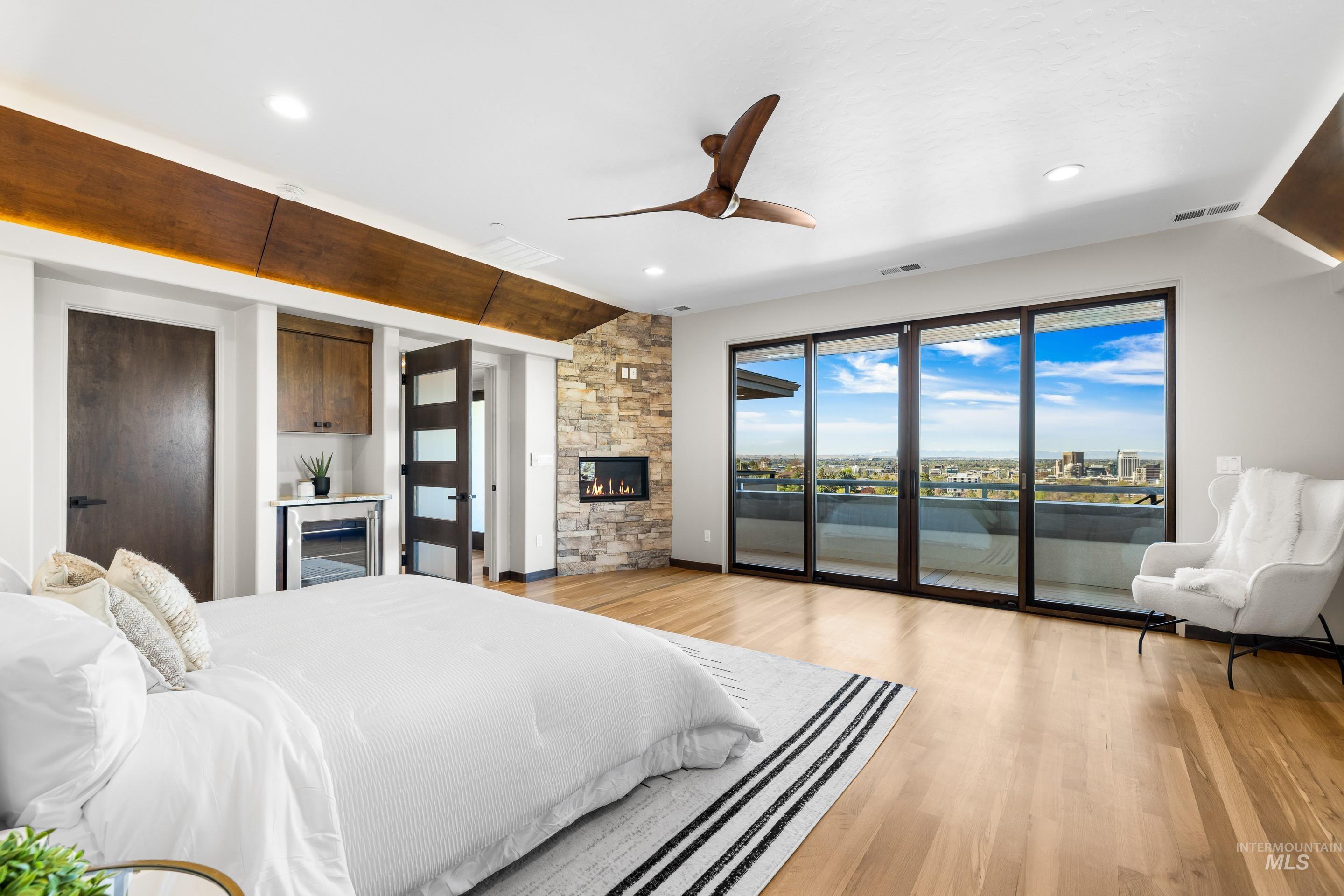 Expansive sliding glass doors opening to an outdoor balcony, stone accent wall with a built-in fireplace, recessed lighting, wood-finish flooring, and a beverage cooler