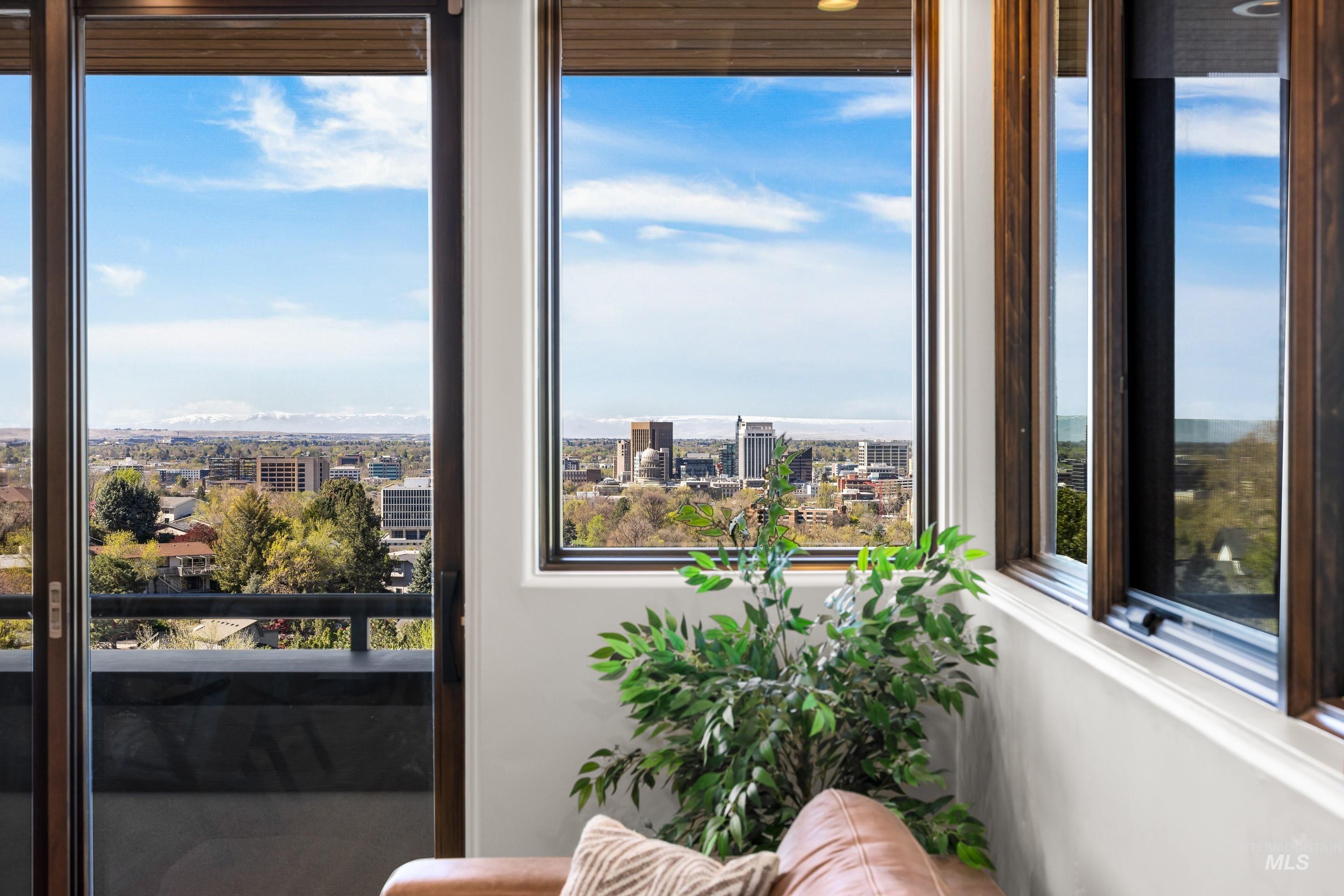 Expansive glass doors and windows frame a cityscape, distant mountains, and mature trees