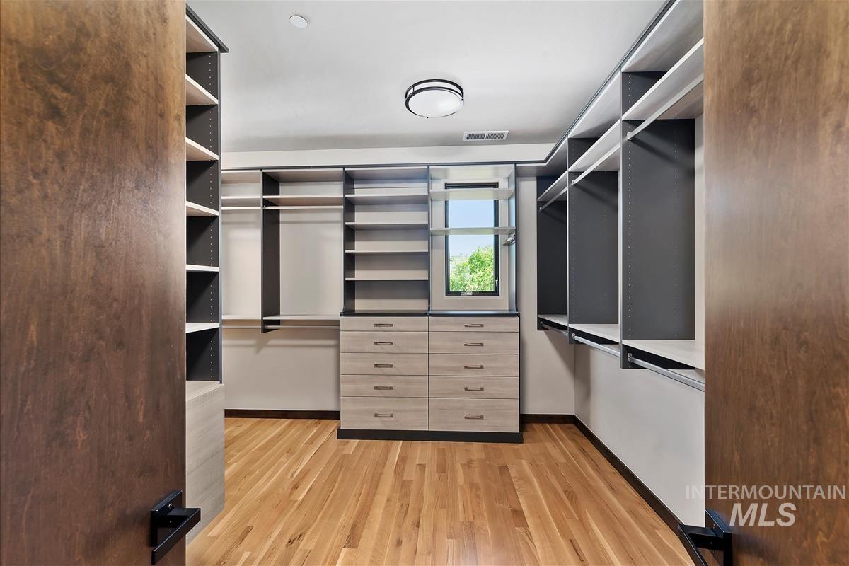 Custom closet system featuring wood-finish flooring, extensive shelving, integrated drawer storage, and a flush-mount ceiling light fixture