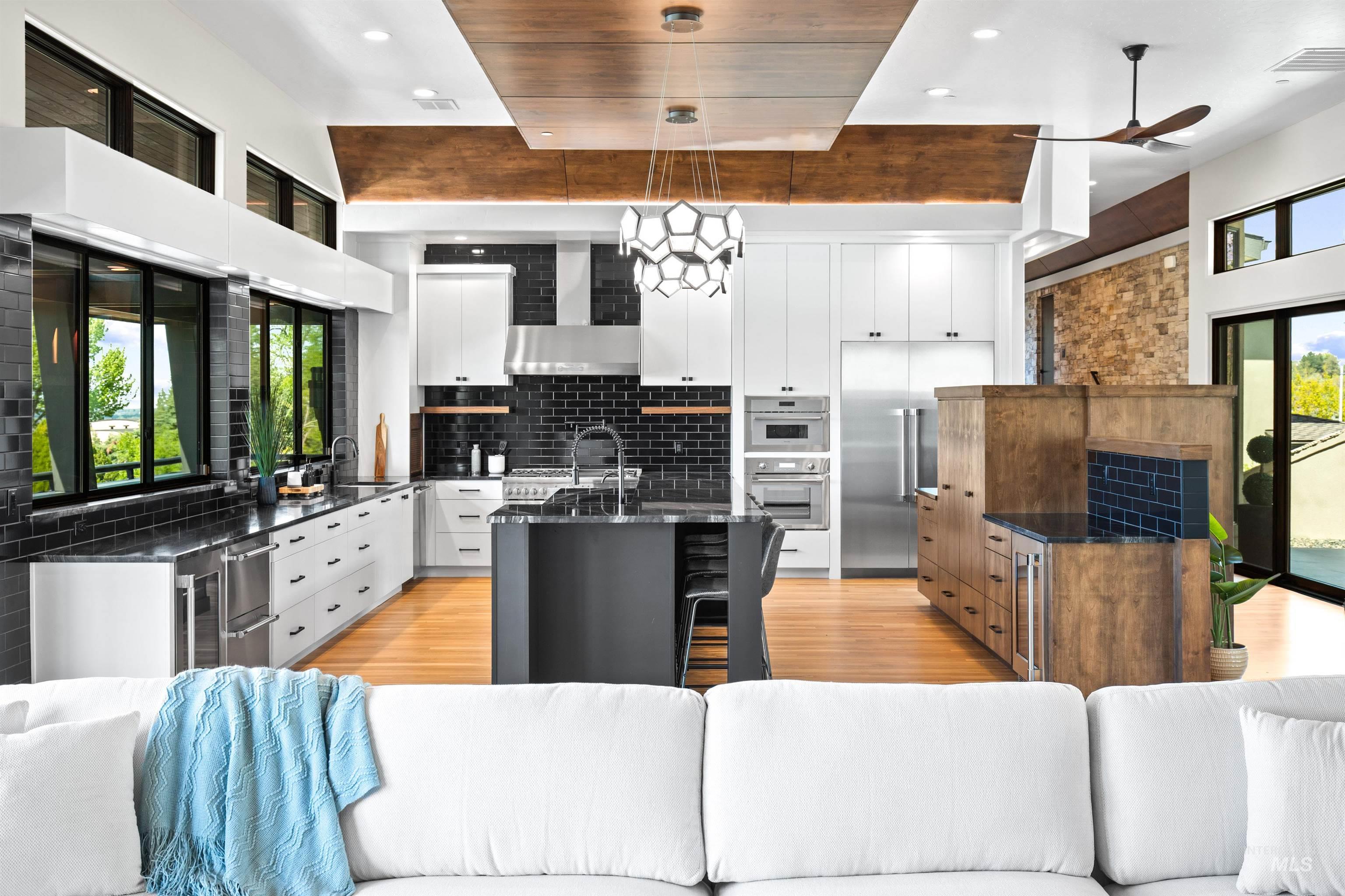 Open-concept kitchen featuring an island, black subway tile backsplash, white and wood-finish cabinetry, stainless steel appliances, and a wood-finish ceiling accent