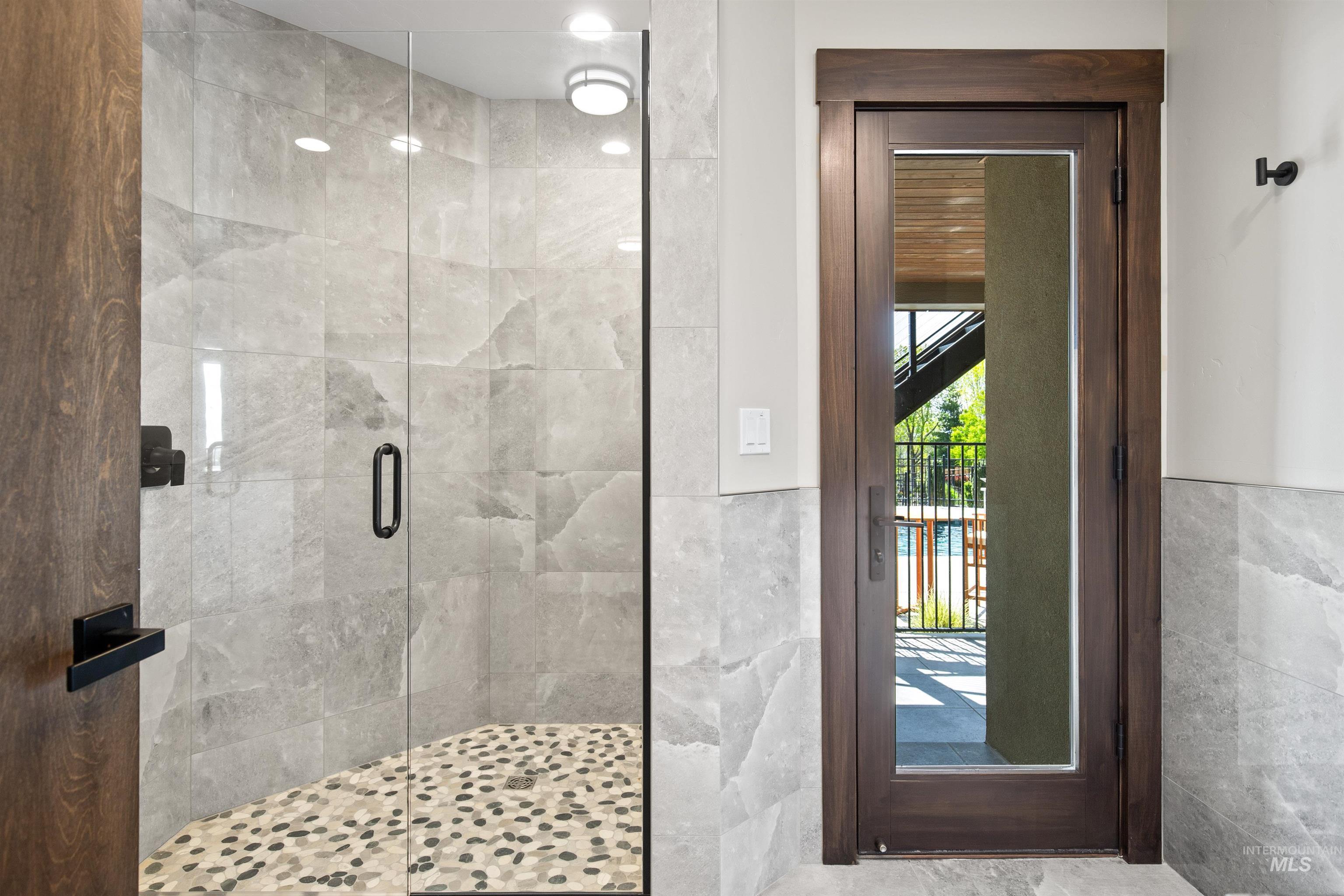 Walk-in shower with clear glass enclosure, natural stone tile walls, and a pebble mosaic floor
