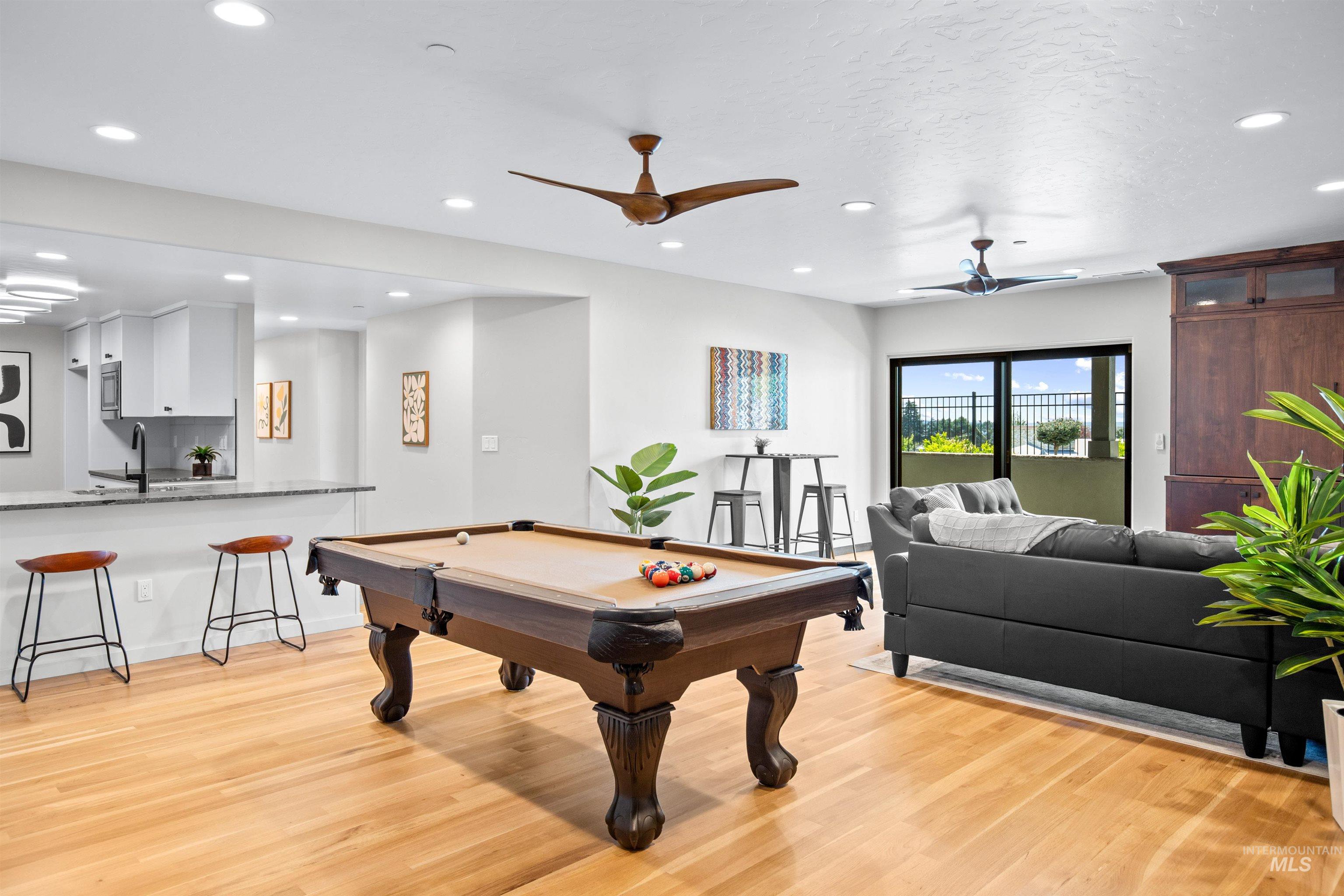 Spacious open-concept room featuring light wood-finish flooring, recessed lighting, and modern ceiling fans