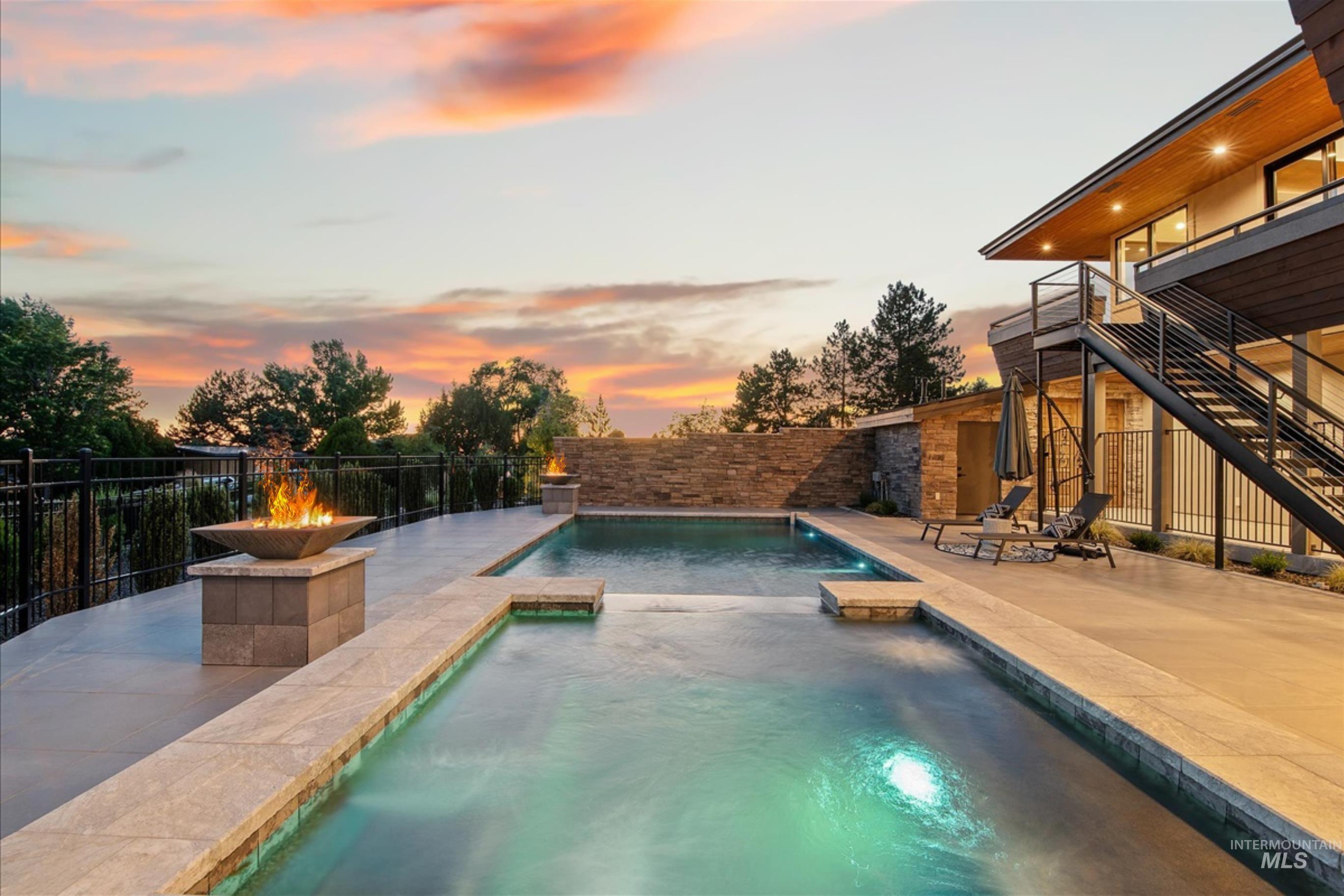 Outdoor living space featuring a multi-level pool with integrated spa, expansive paver patio, two fire features, and a stacked stone privacy wall