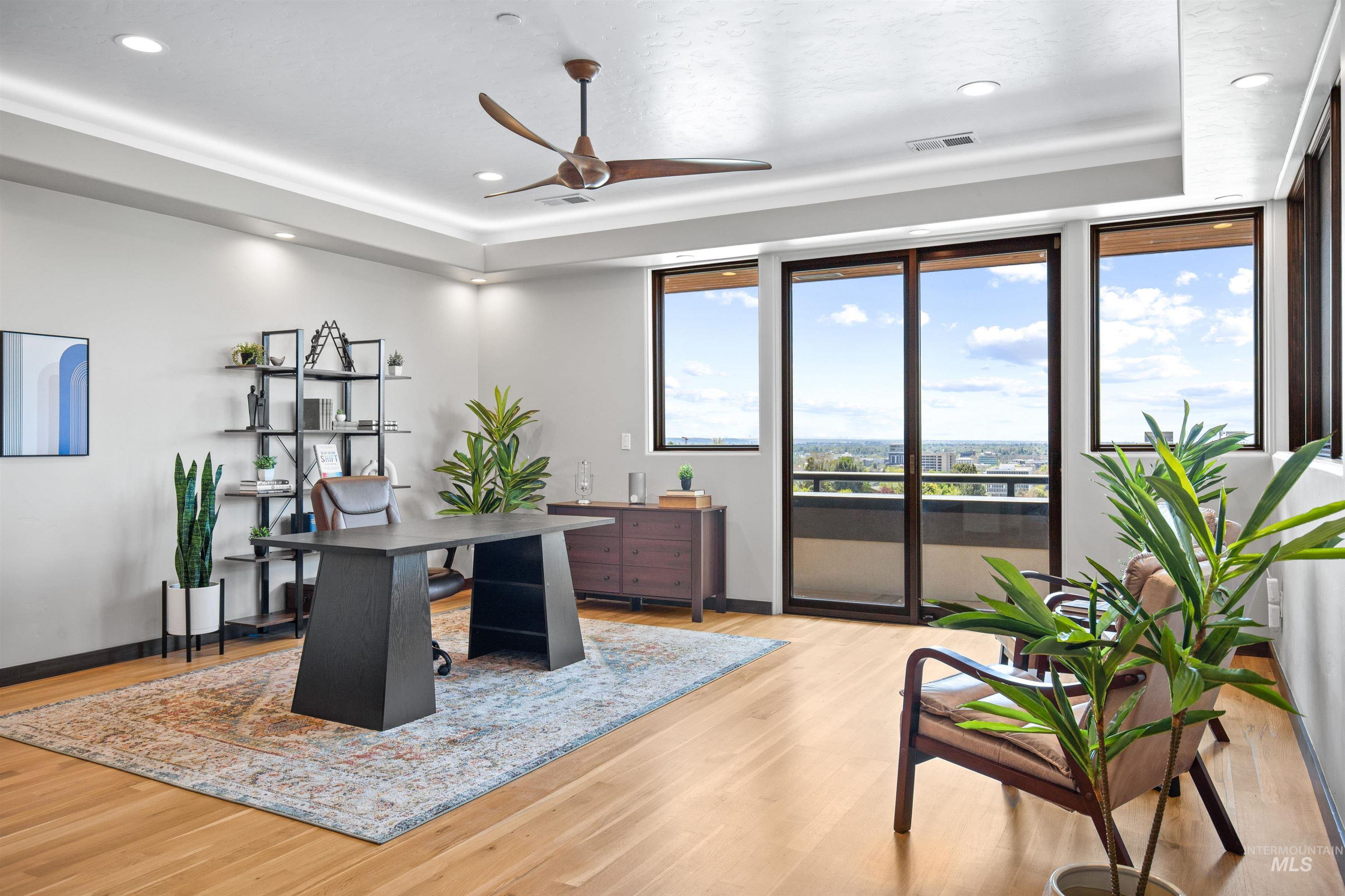 Expansive room featuring wood-finish flooring, a tray ceiling with recessed lighting, and a modern ceiling fan