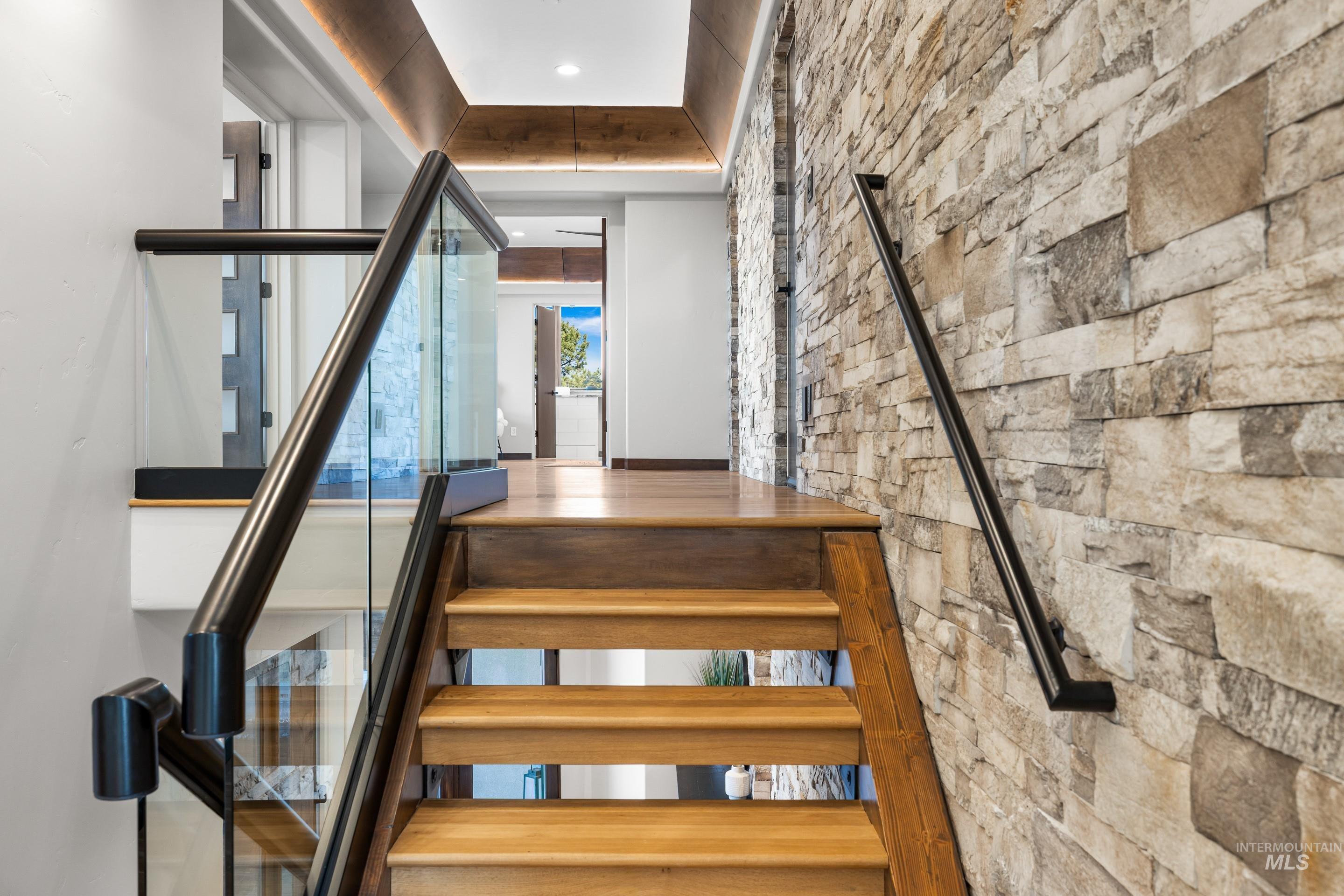 Hardwood staircase featuring a glass and metal railing, complemented by a stone accent wall